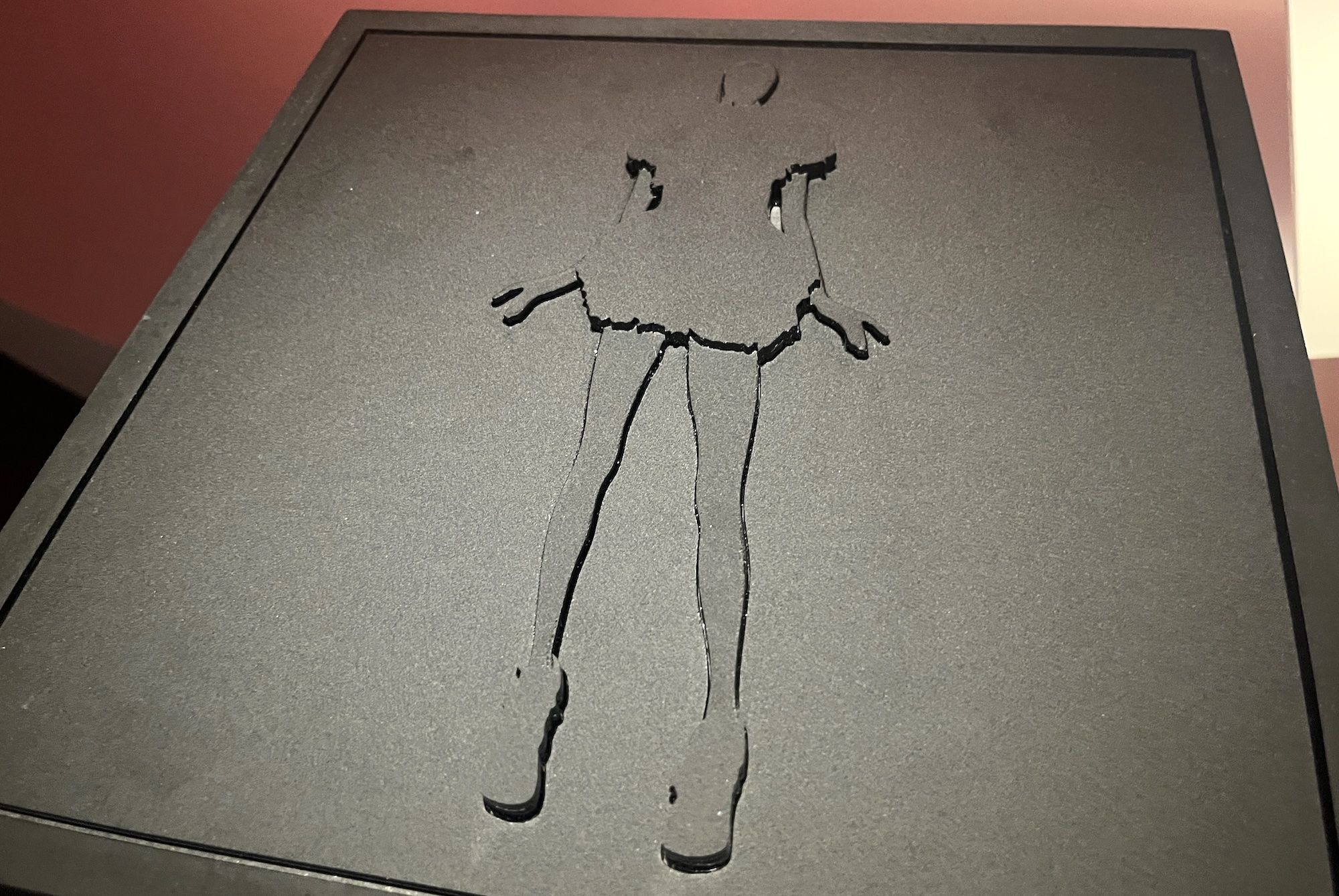 A black square with a raised outline of woman wearing a short dress.