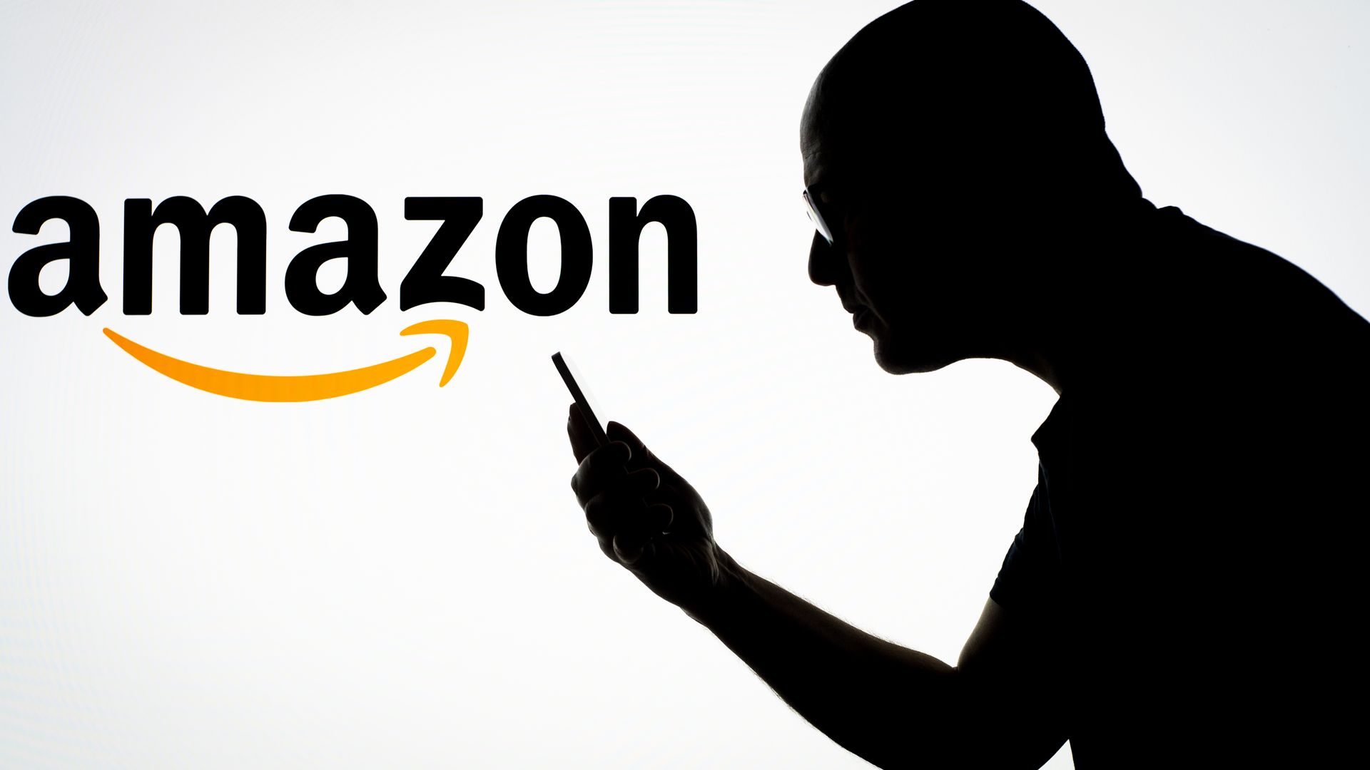 An Amazon logo with a shadow of a man looking at his phone.