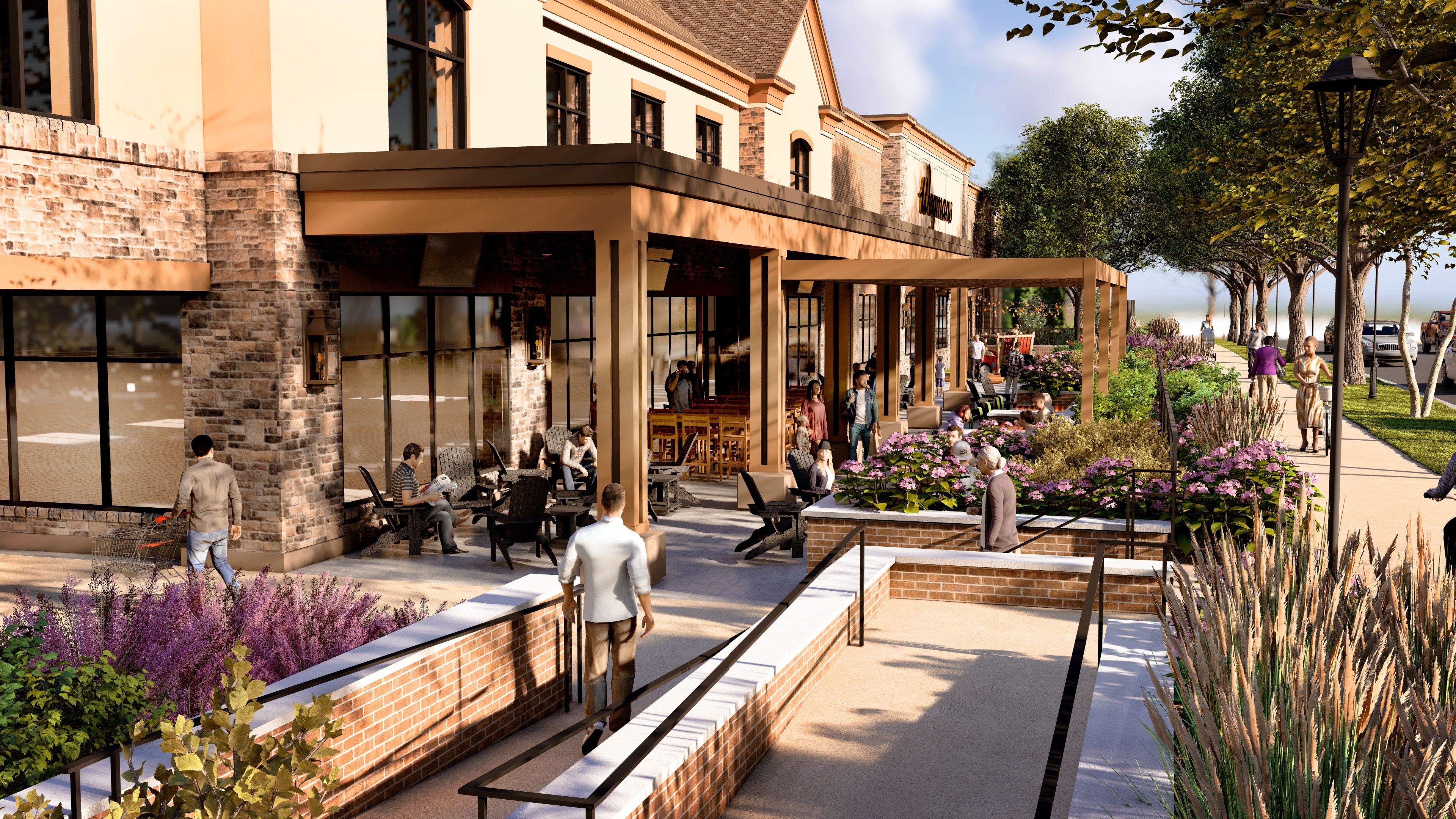 Outdoor cafe area with people sitting and walking near a brick building, surrounded by purple flowers, shrubs, trees, and a sidewalk with pedestrians on a sunny day.