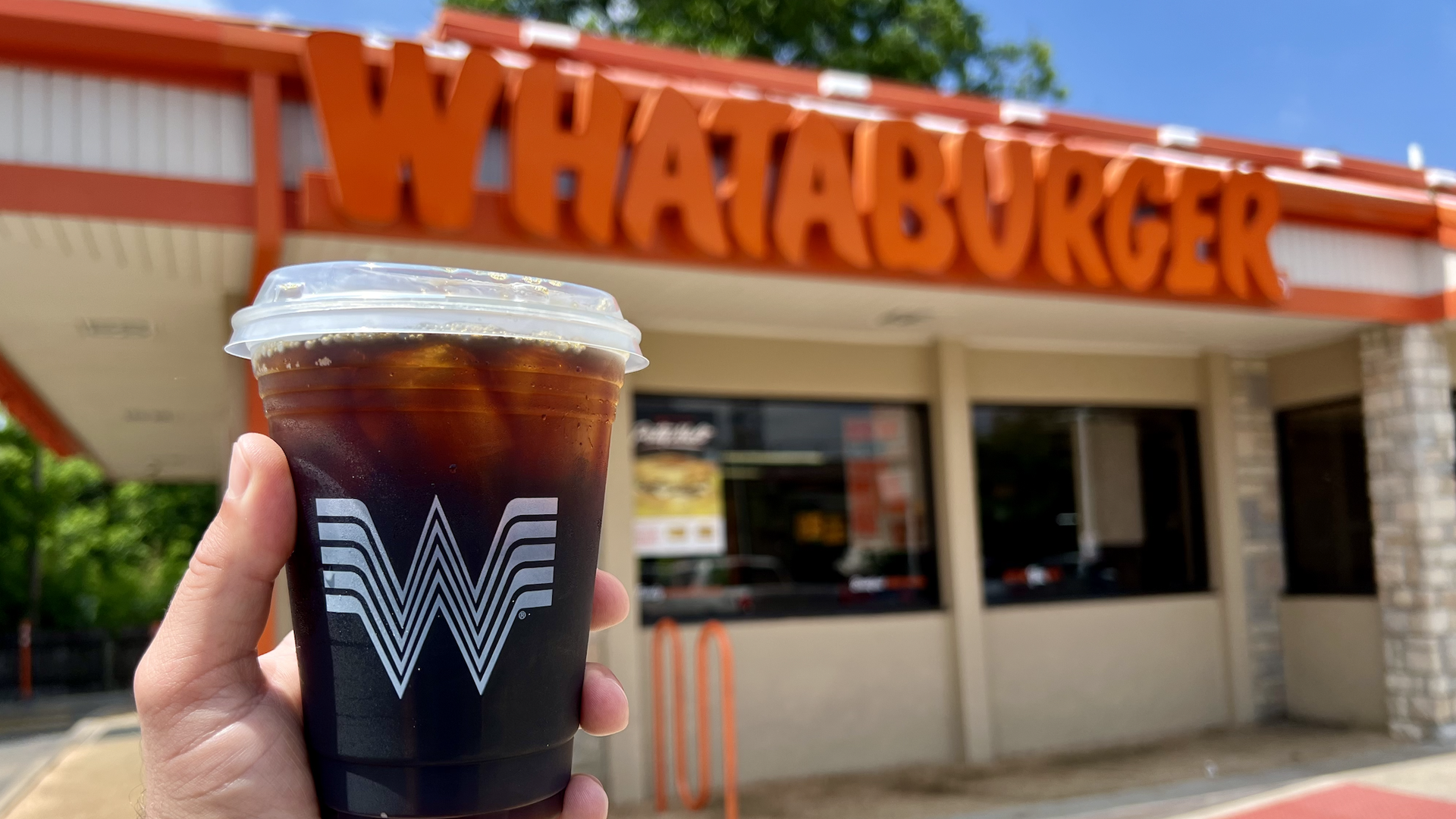 A photo of a Whataburger iced coffee with a "Whataburger" sign in the background.