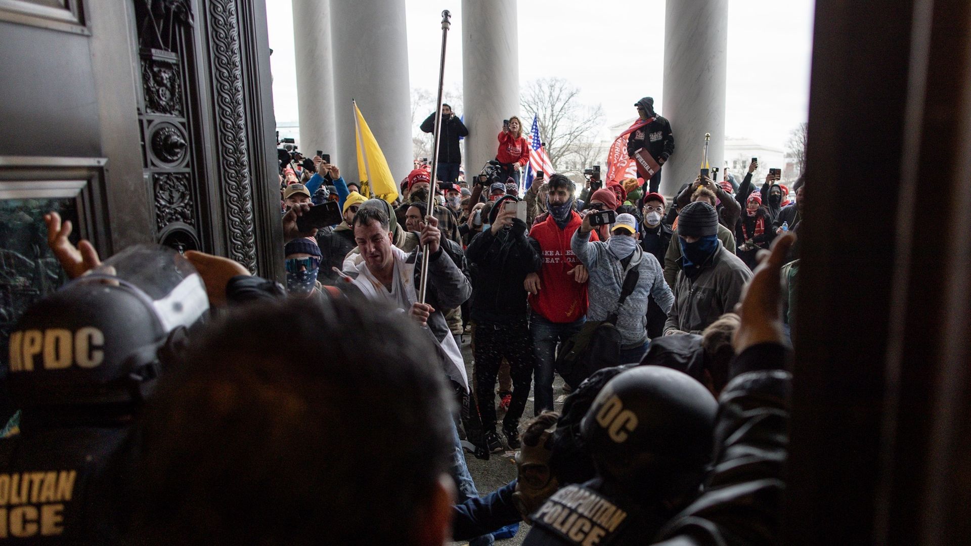 Photo of a crowd of Trump supporters standing outside an open door into the Capitol building, holding pro-Trump signs as they look at security officers