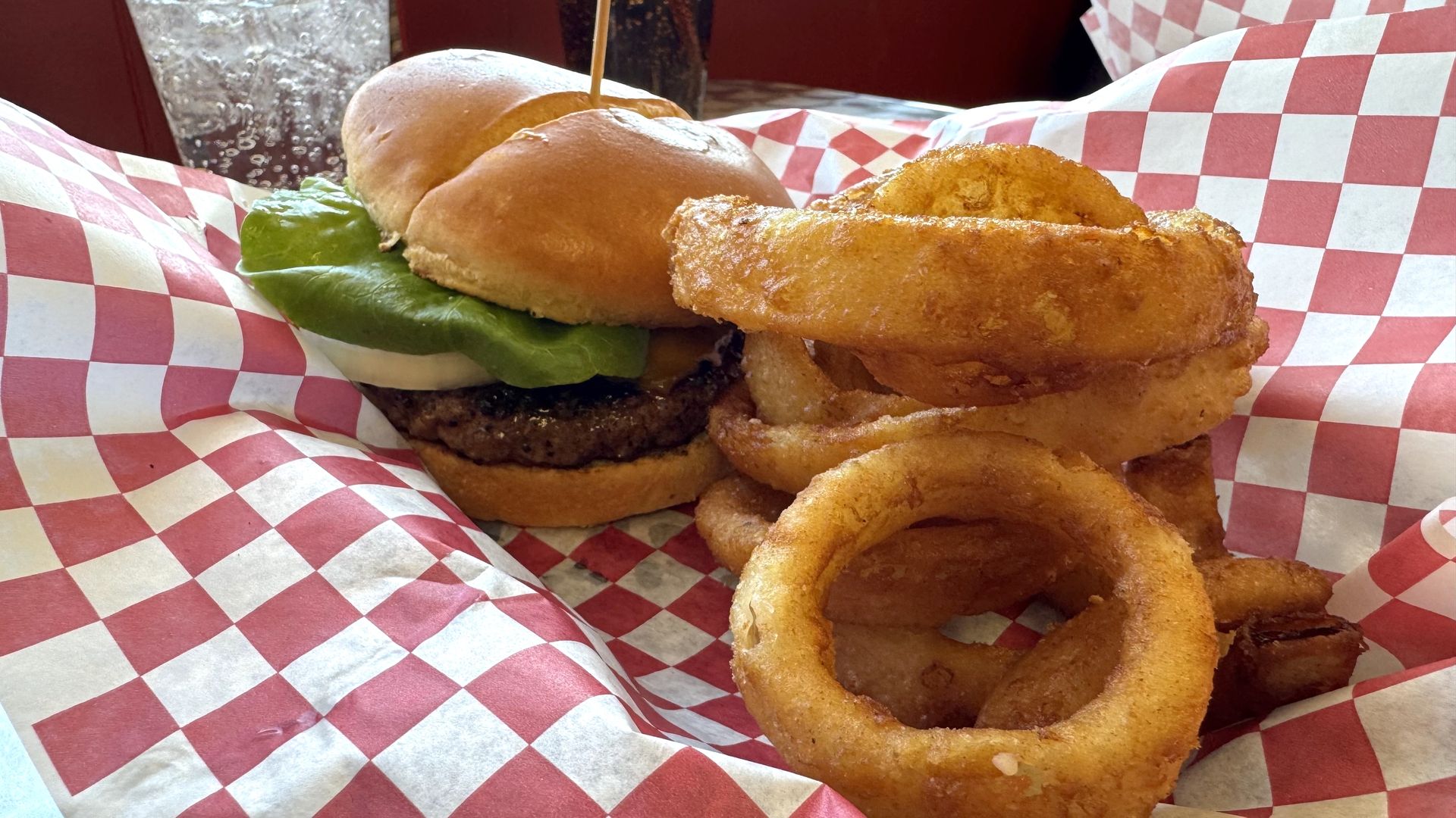 A burger and onion rings on red and white checked paper.