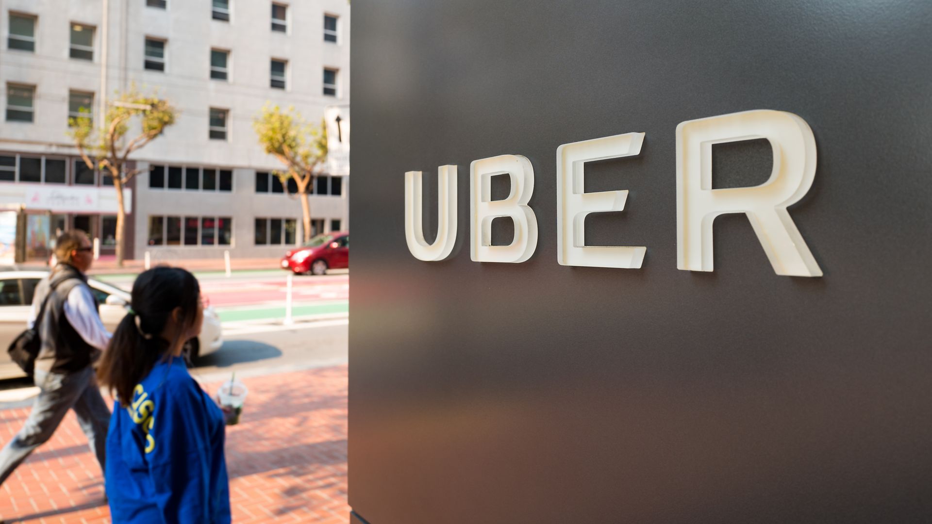 People walk down Market Street past sign with logo at the headquarters of Uber in the South of Market neighborhood of San Francisco, California, October 13, 2017.