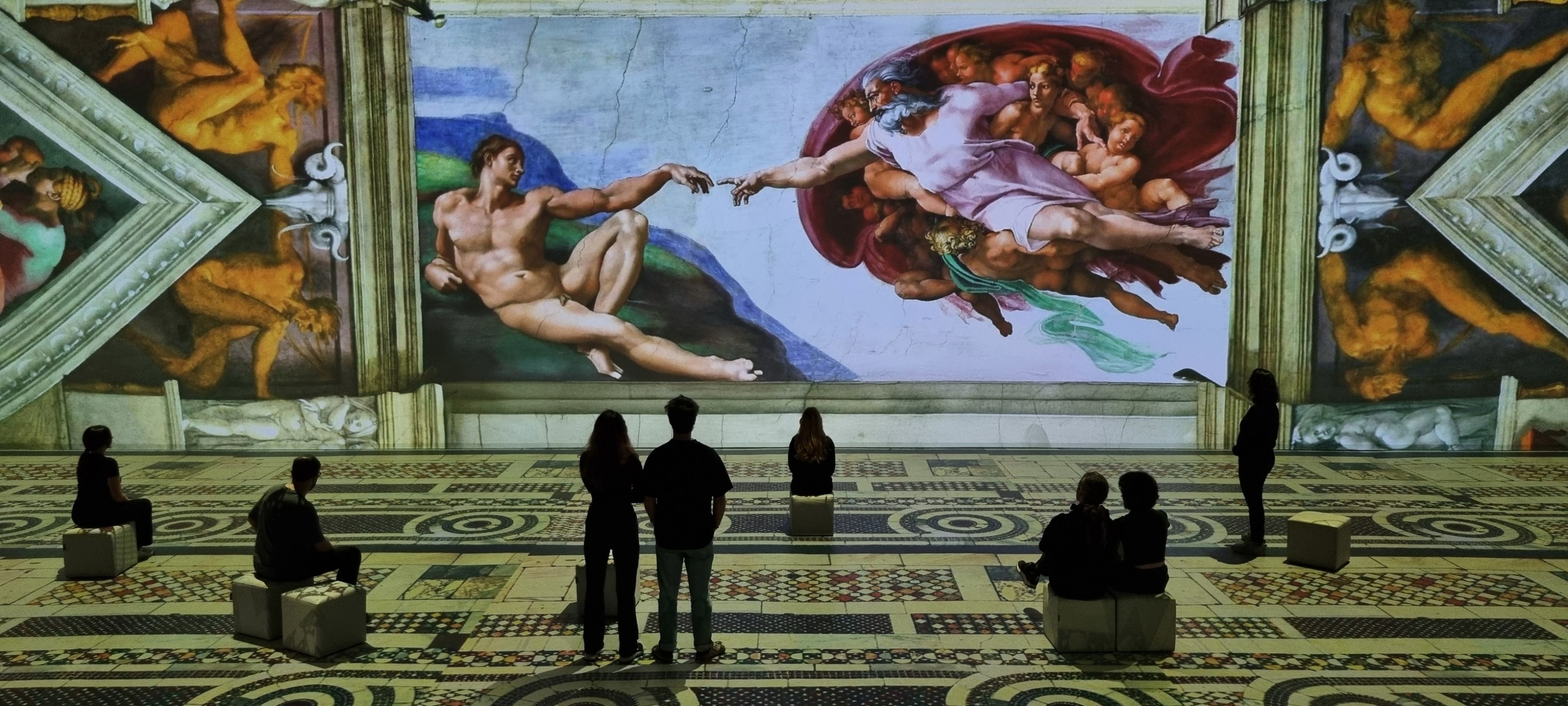 Inside a museum, a large mural of Michelangelo's "The Creation of Adam" covers the wall: Adam reaches toward God among angels, framed by ornate arches; visitors sit and stand on a patterned floor.