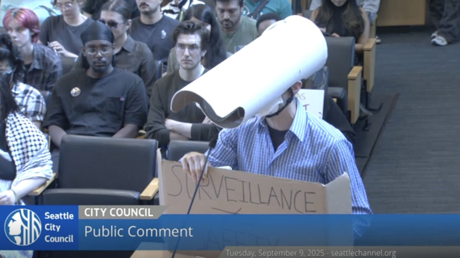 A person wearing a surveillance camera mask speaks at a city council meeting in Seattle. 