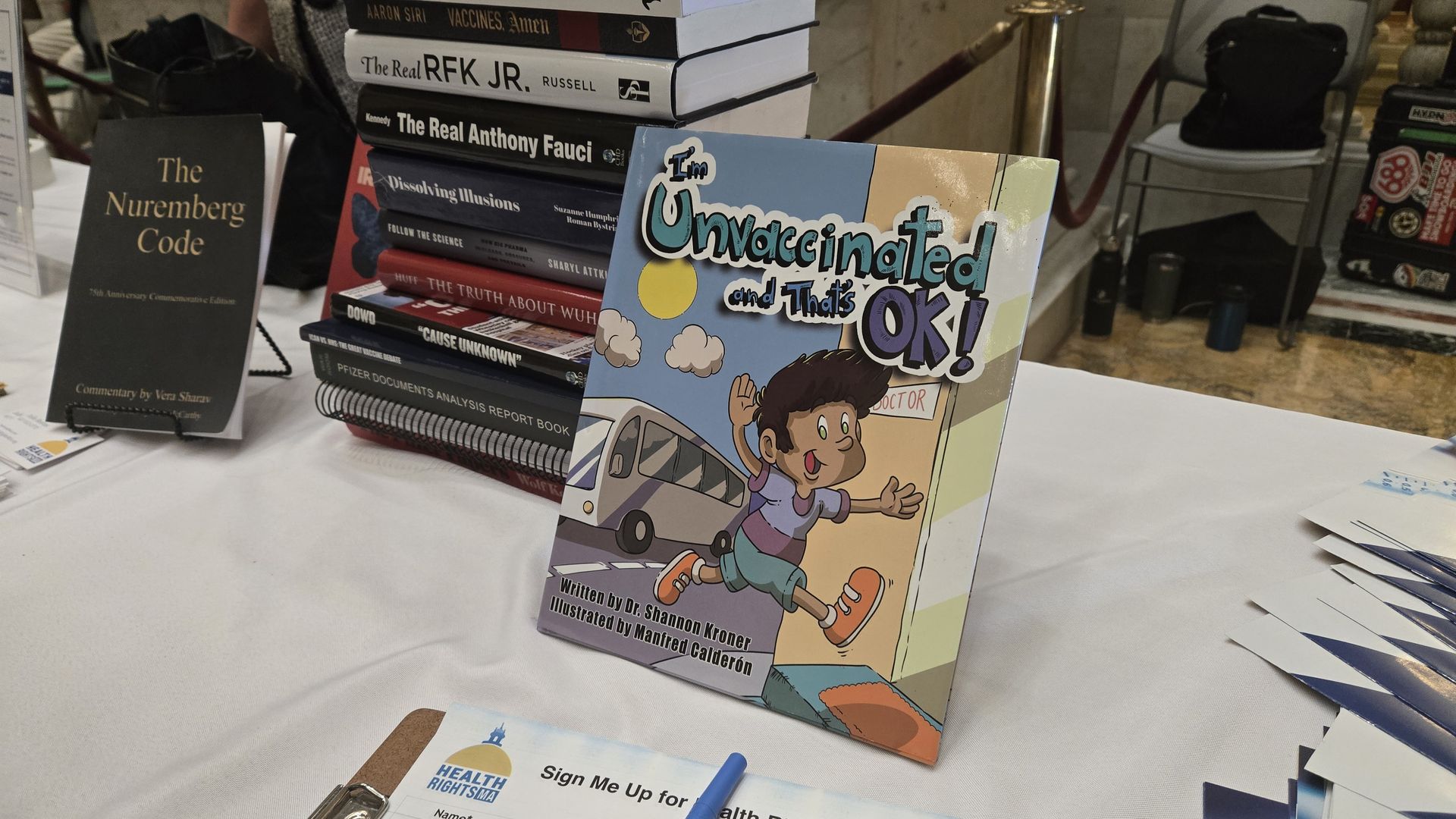 Table display with books including "I'm Unvaccinated and That's OK!", "The Nuremberg Code", and others, promoting health rights and vaccine skepticism.
