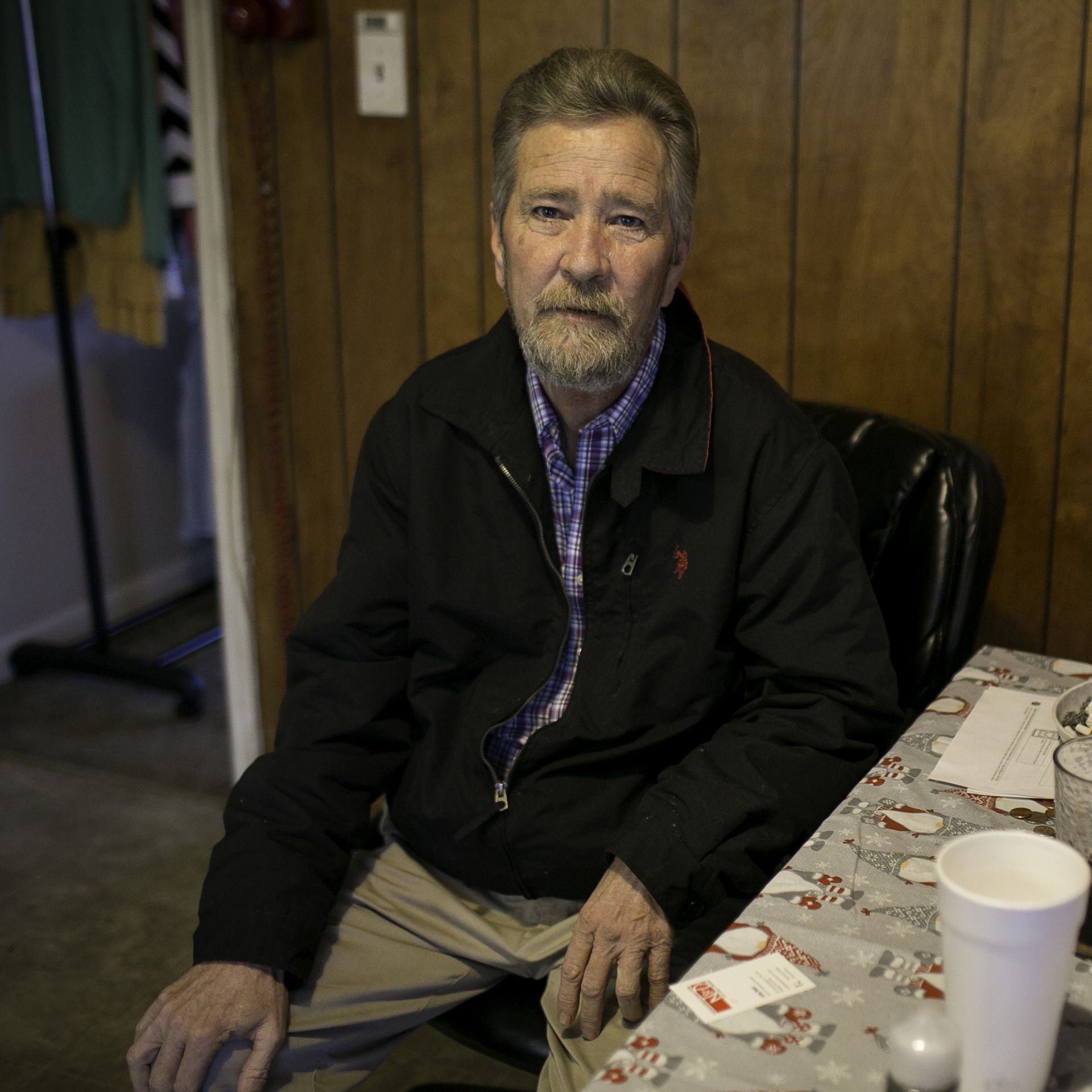 photo of a man named McCrae Dowless sitting at a kitchen table with wood paneling behind him and cigarettes in an ashtray