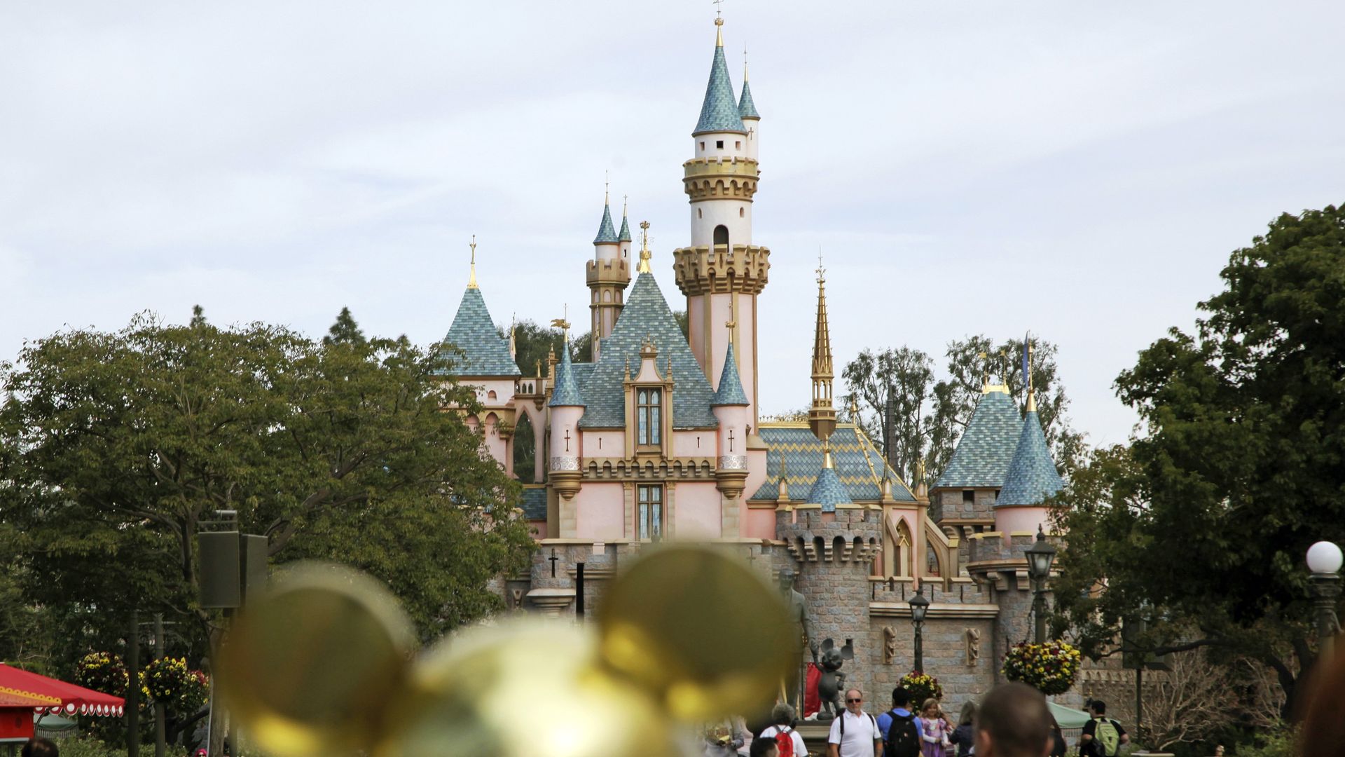 Disneyland castles with a person wearing Mickey ears in the foreground.
