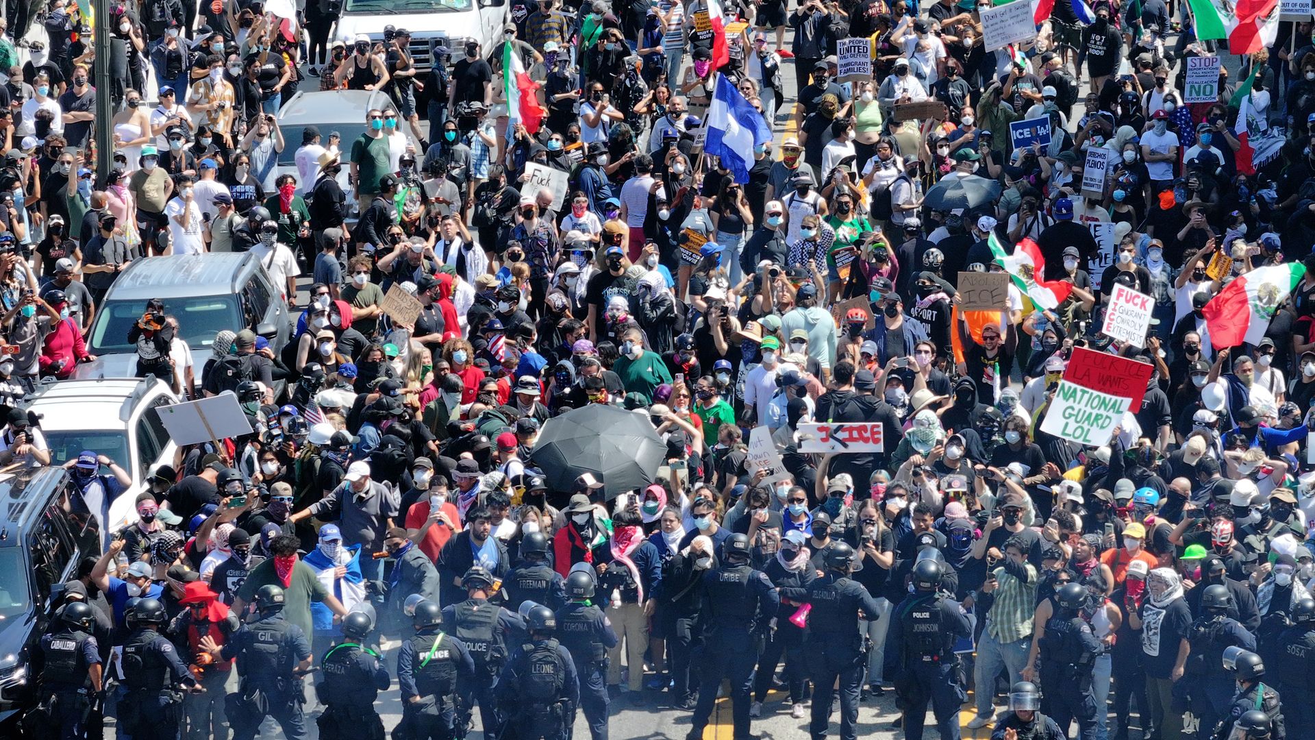Hundreds of protesters gather in LA, waving flags and signs as law enforcement stands guard.
