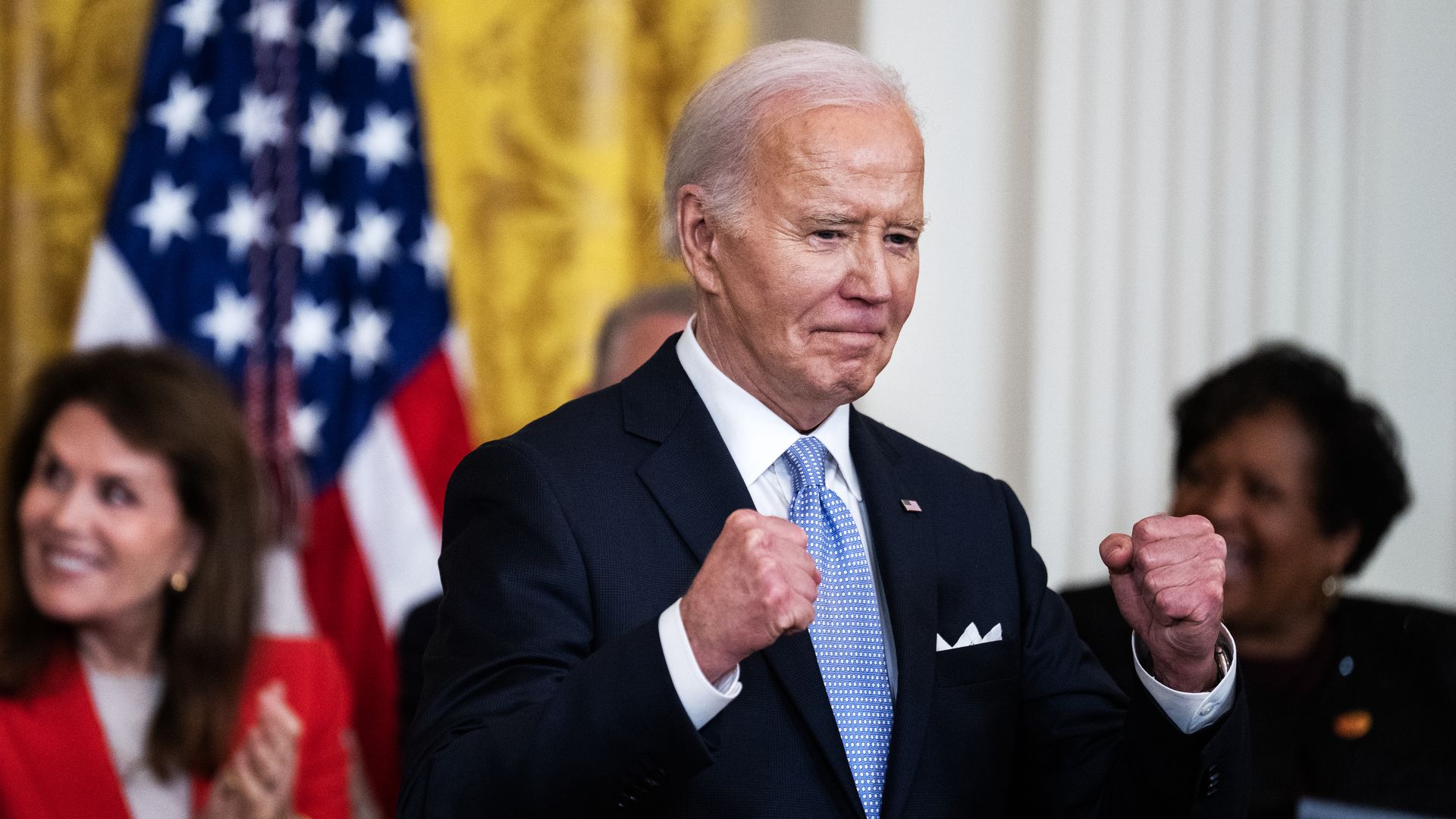 President Biden, wearing a dark blue suit, white shirt and light blue tie, holding up his fists.