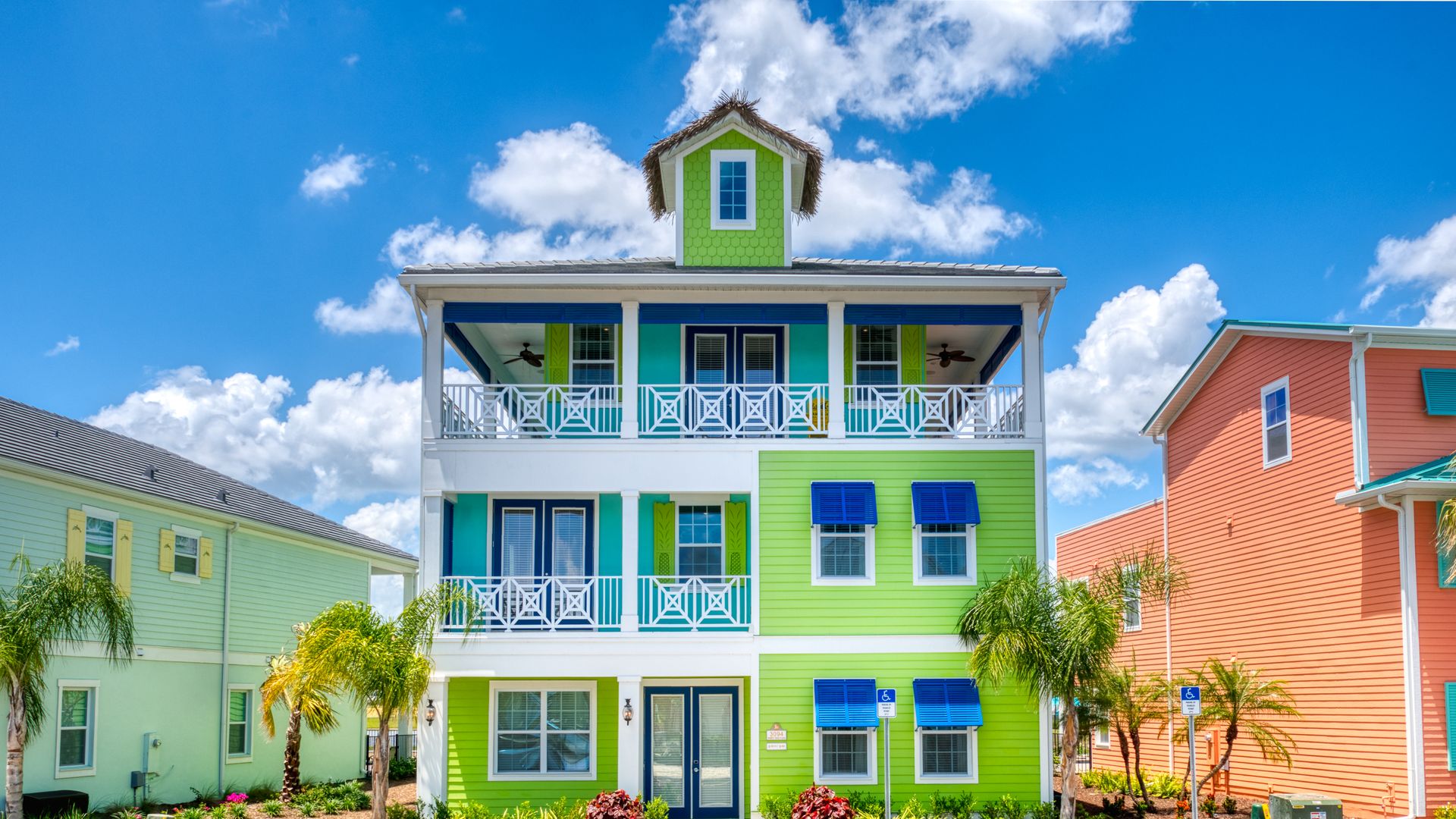 A bright, lime green, 3-story building with white balconies and blue shutters and palm trees in front. 