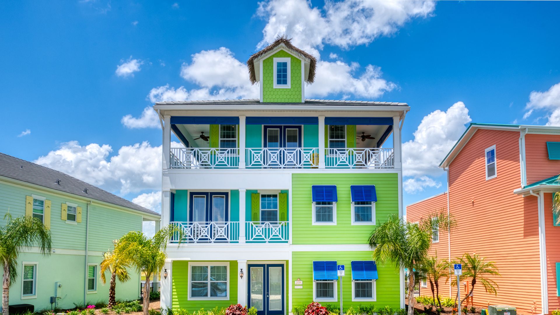 A bright, lime green, 3-story building with white balconies and blue shutters and palm trees in front.