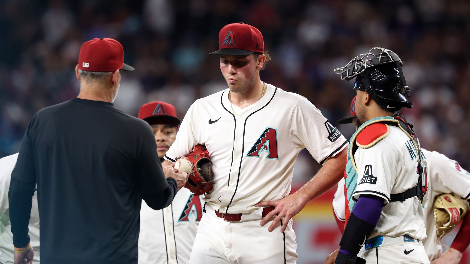 Brandon Pfaadt hands the baseball to Torey Lovullo while several other Arizona Diamondbacks players look on near the pitcher's mound.