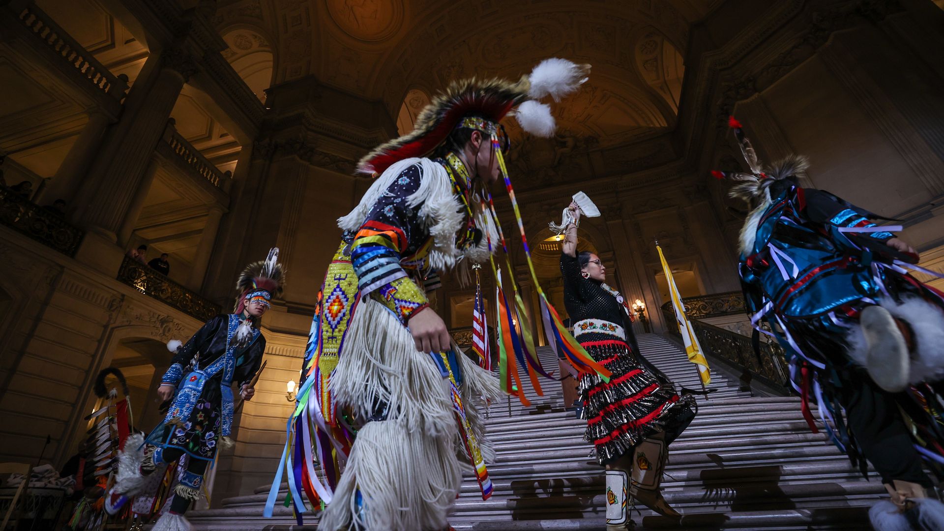 Photo of Indigenous people wearing traditional garb walking in the San Francisco City Hall