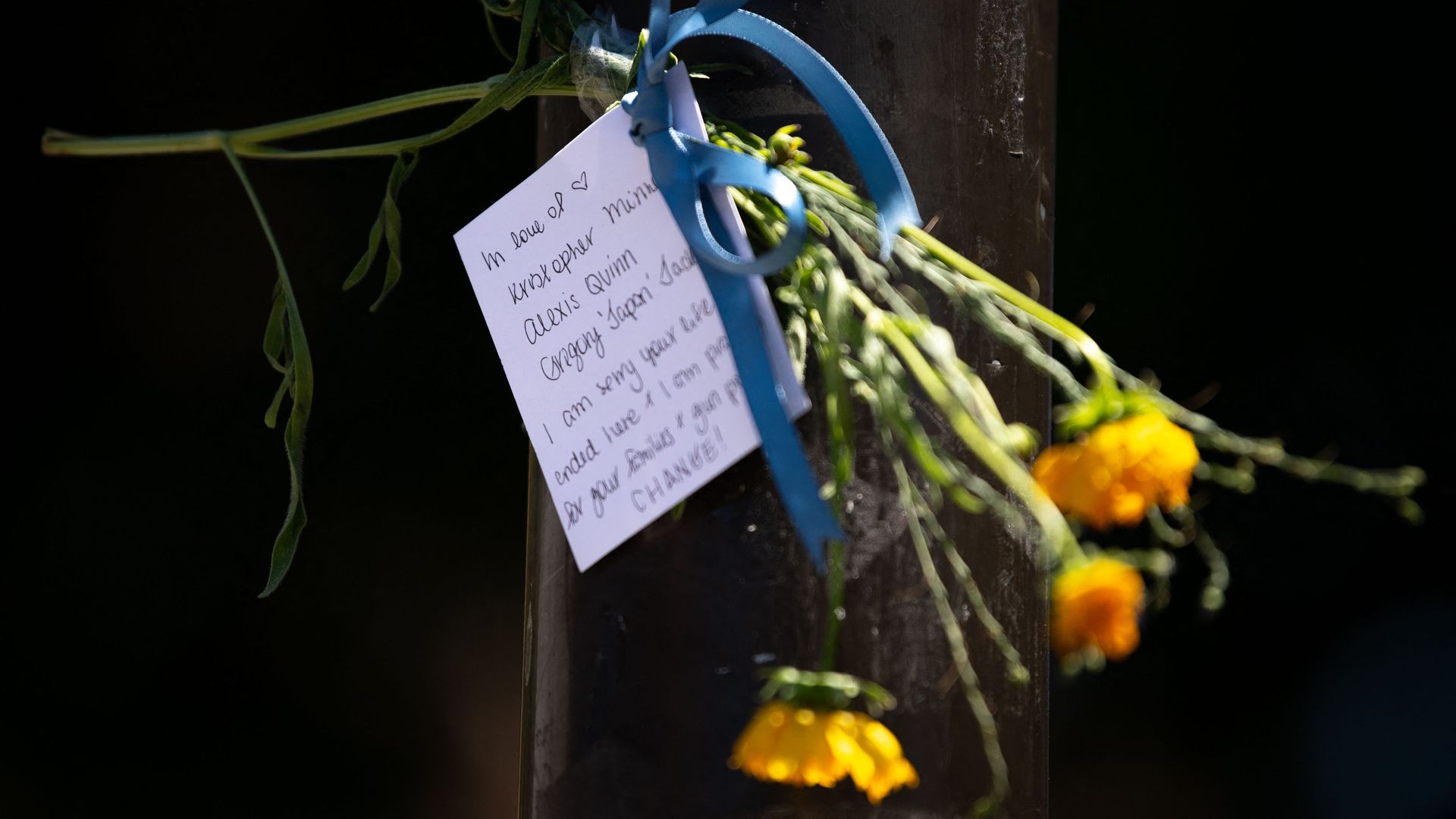 A note and flowers honoring the victims of a mass shooting in South Philadelphia are taped to a traffic light post 