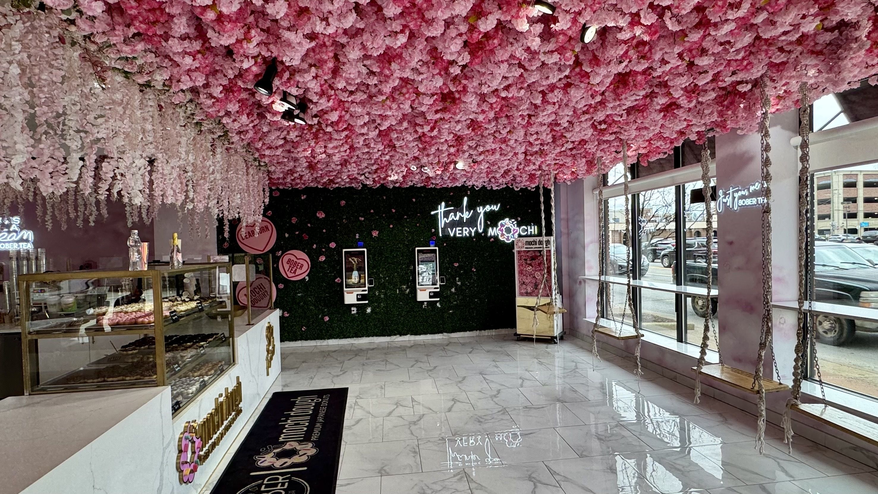 The interior of the dessert spot has its ceiling covered with pink flowers and swings hanging from the ceiling.