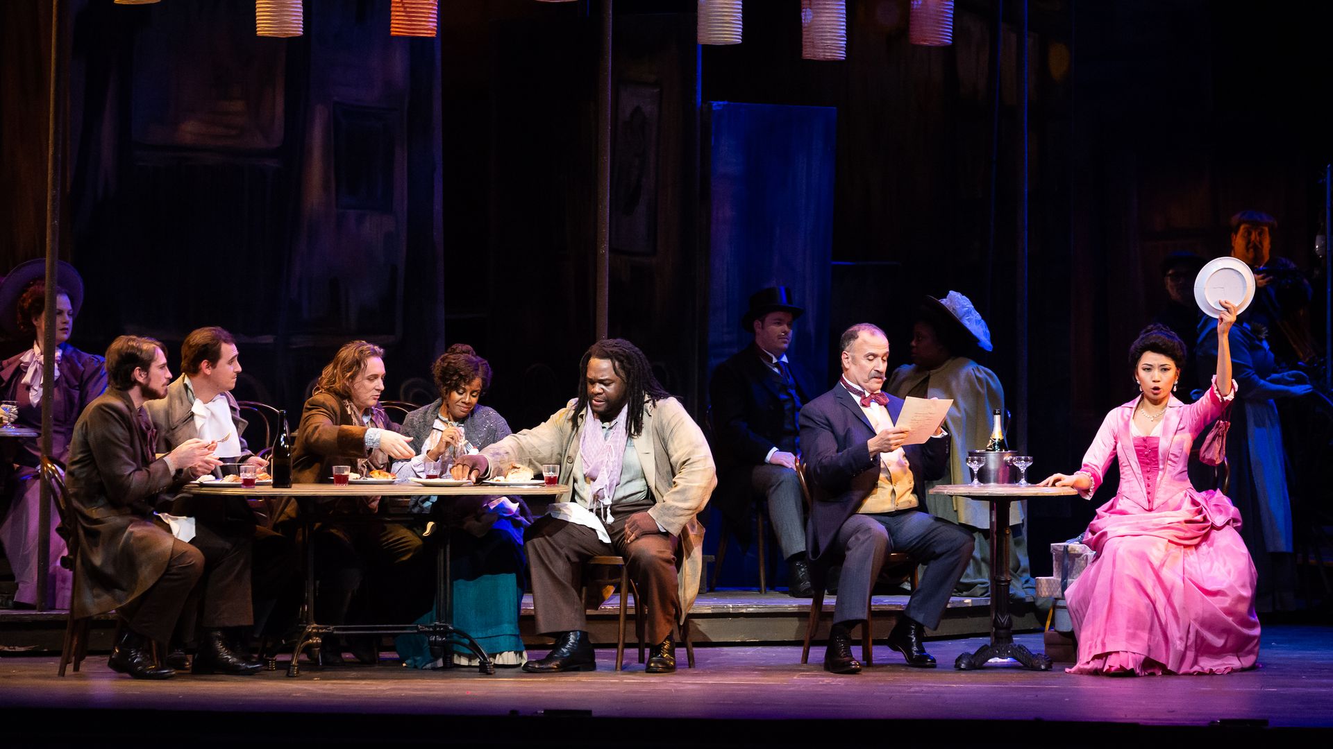 Photo of a group of people on stage, sitting at tables. 