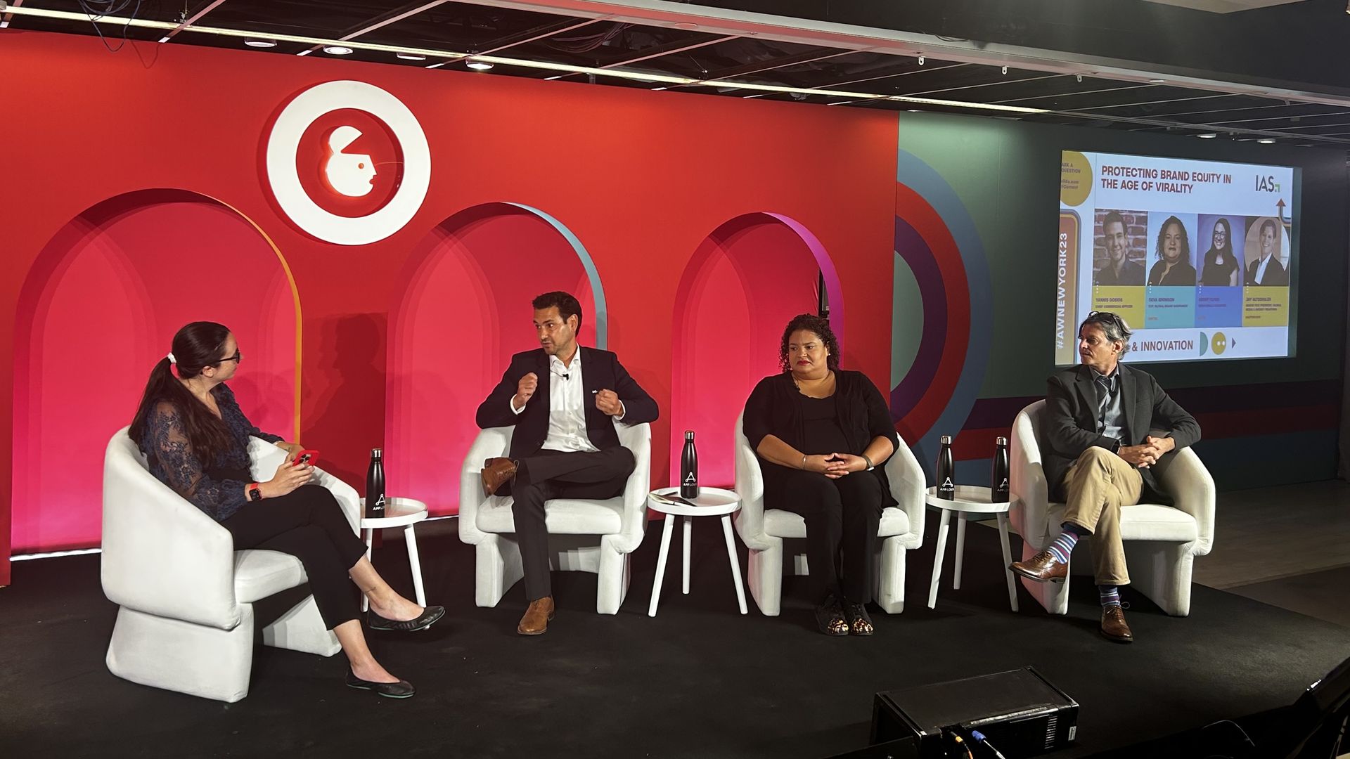 Kerry Flynn, Yannis Dosios, Deva Bronson and Jay Altschuler all seated in white chairs in front of a red background