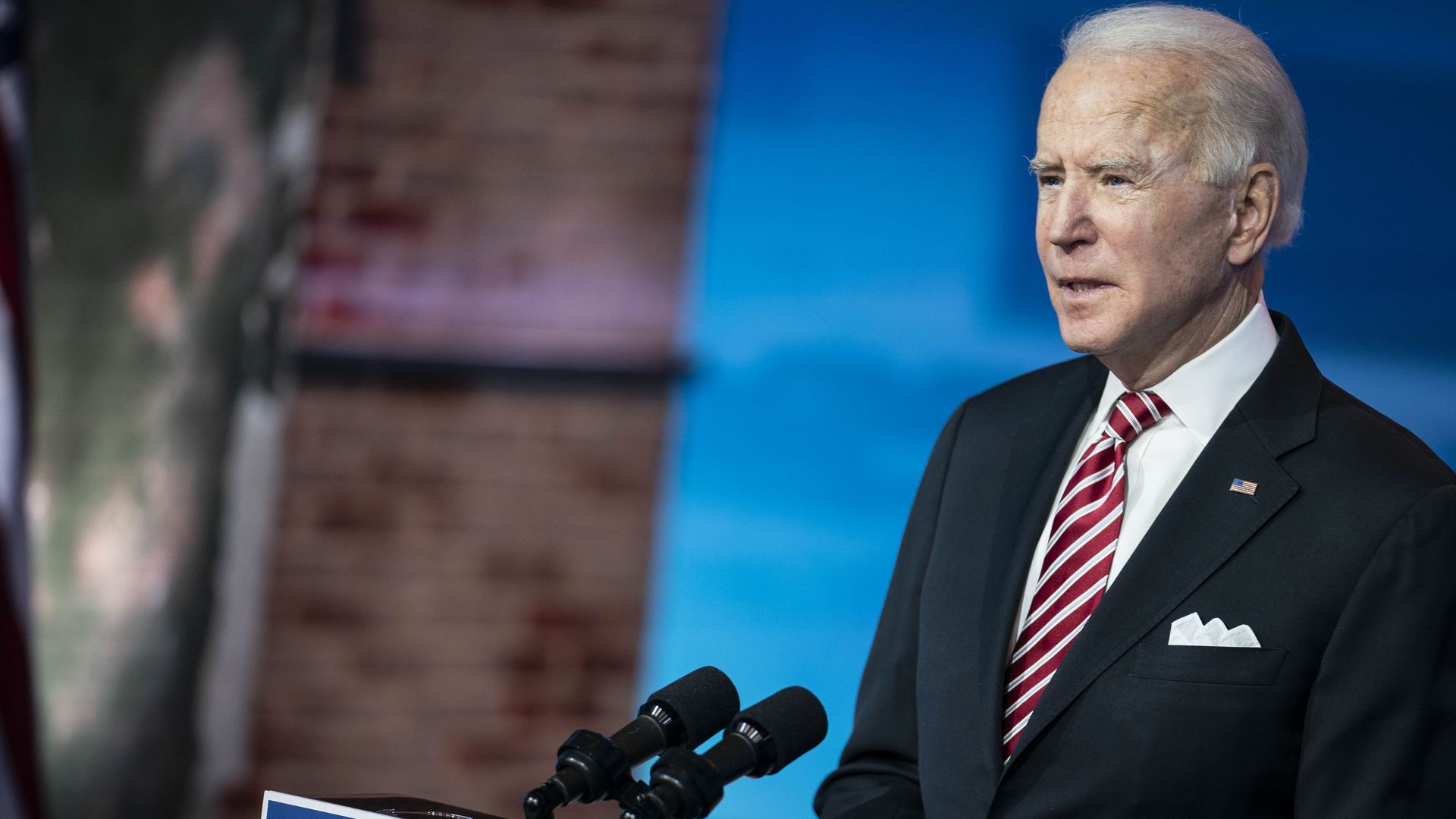 Photo of Joe Biden in a suit standing behind a podium with microphones