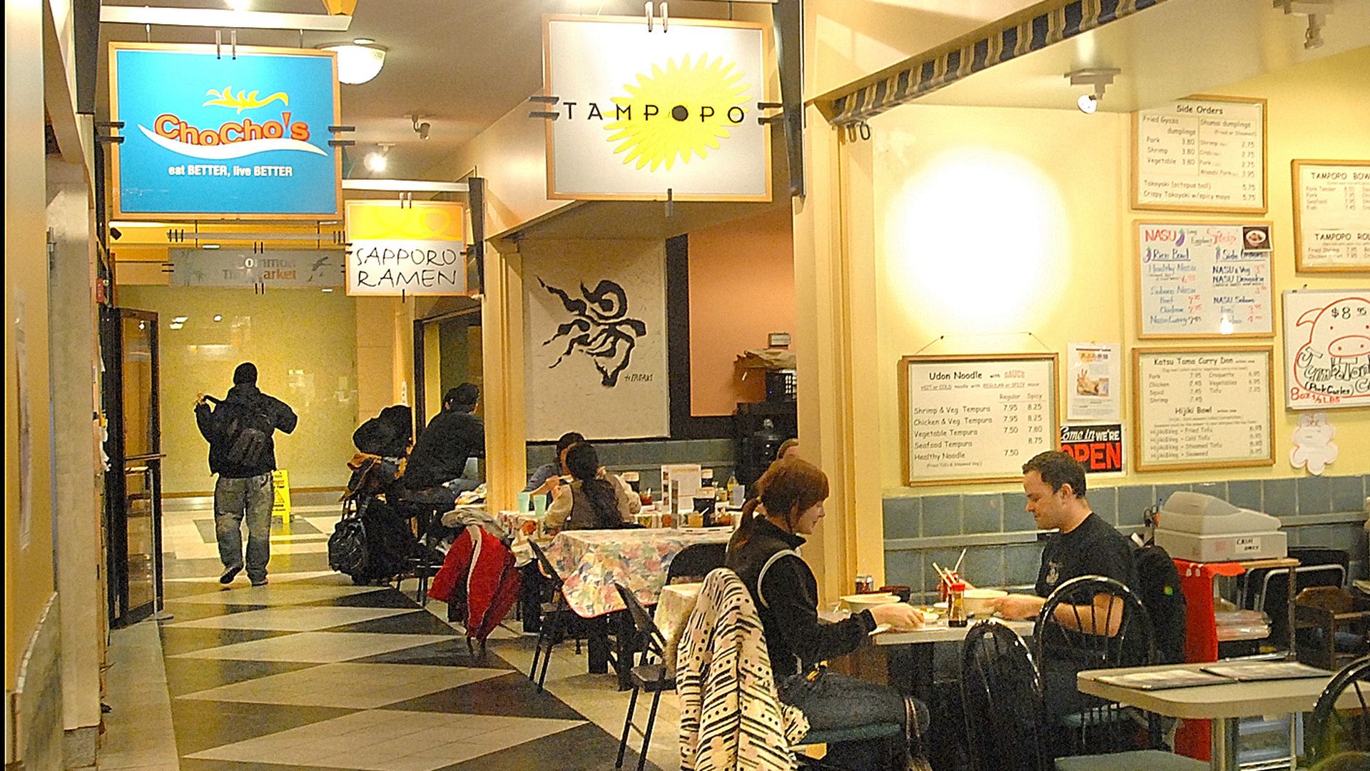 People sit at tables inside the Porter Exchange food court in Cambridge, Mass., with several restaurant counters visible in the background.