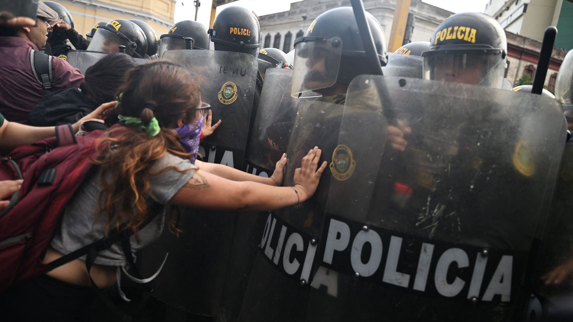 a young person in pigtails in  Peru pushes against a row of police officers in riot gear