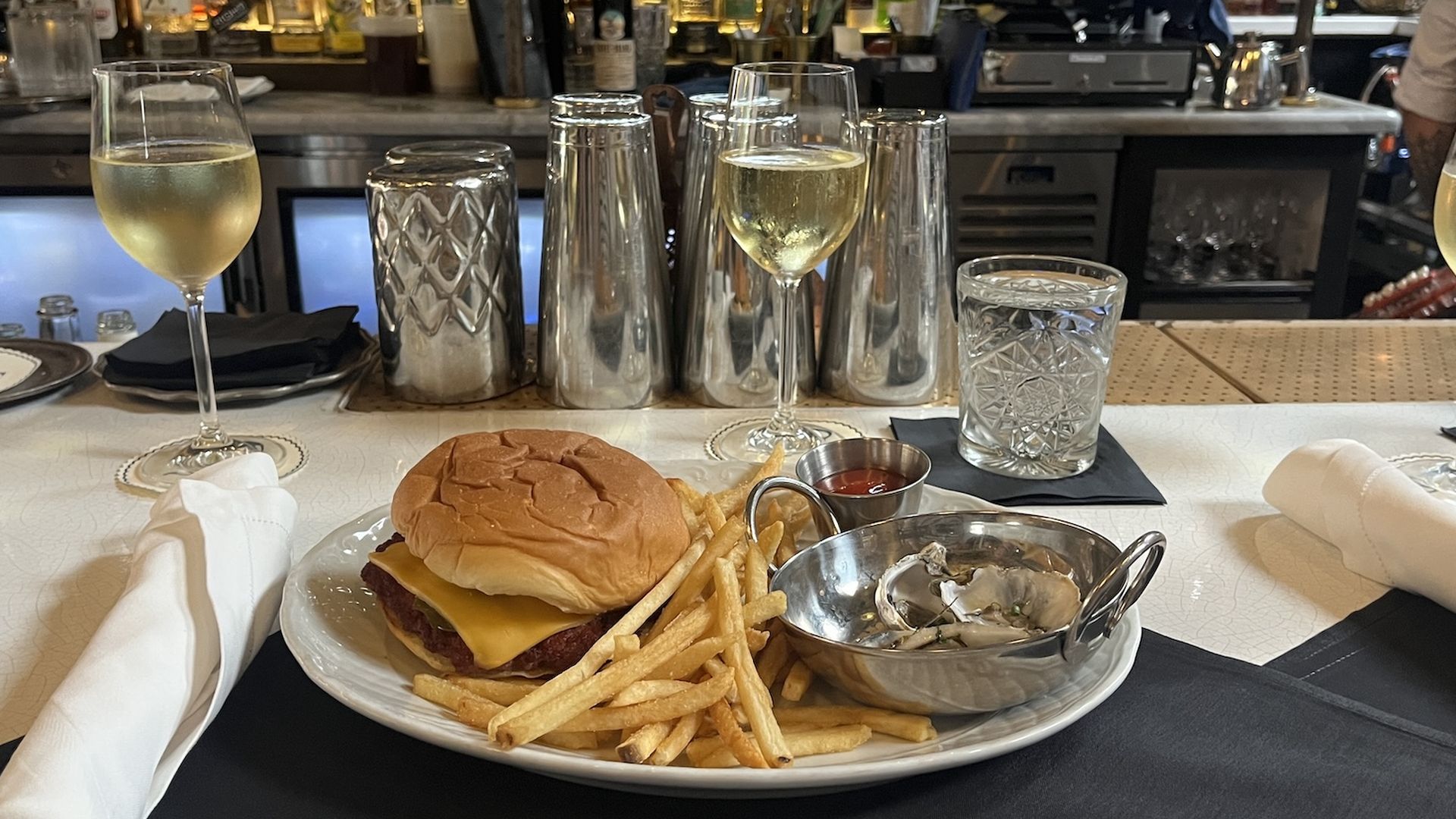 A plate with a cheeseburger, fries and oysters, plus a glass of champagne sitting on a bar countertop.