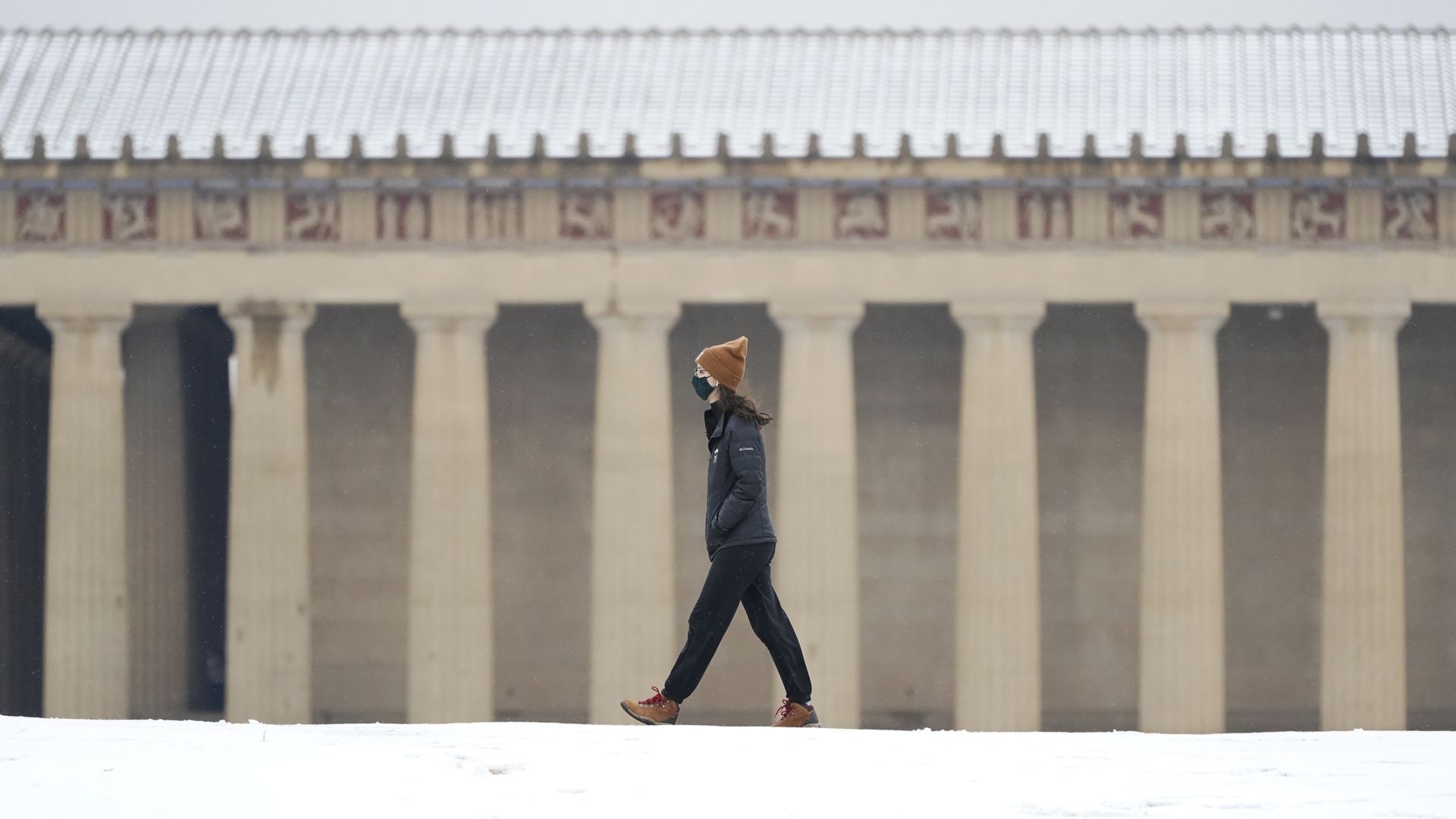 A woman walking outside The Parthenon in Nashville after a snowfall.