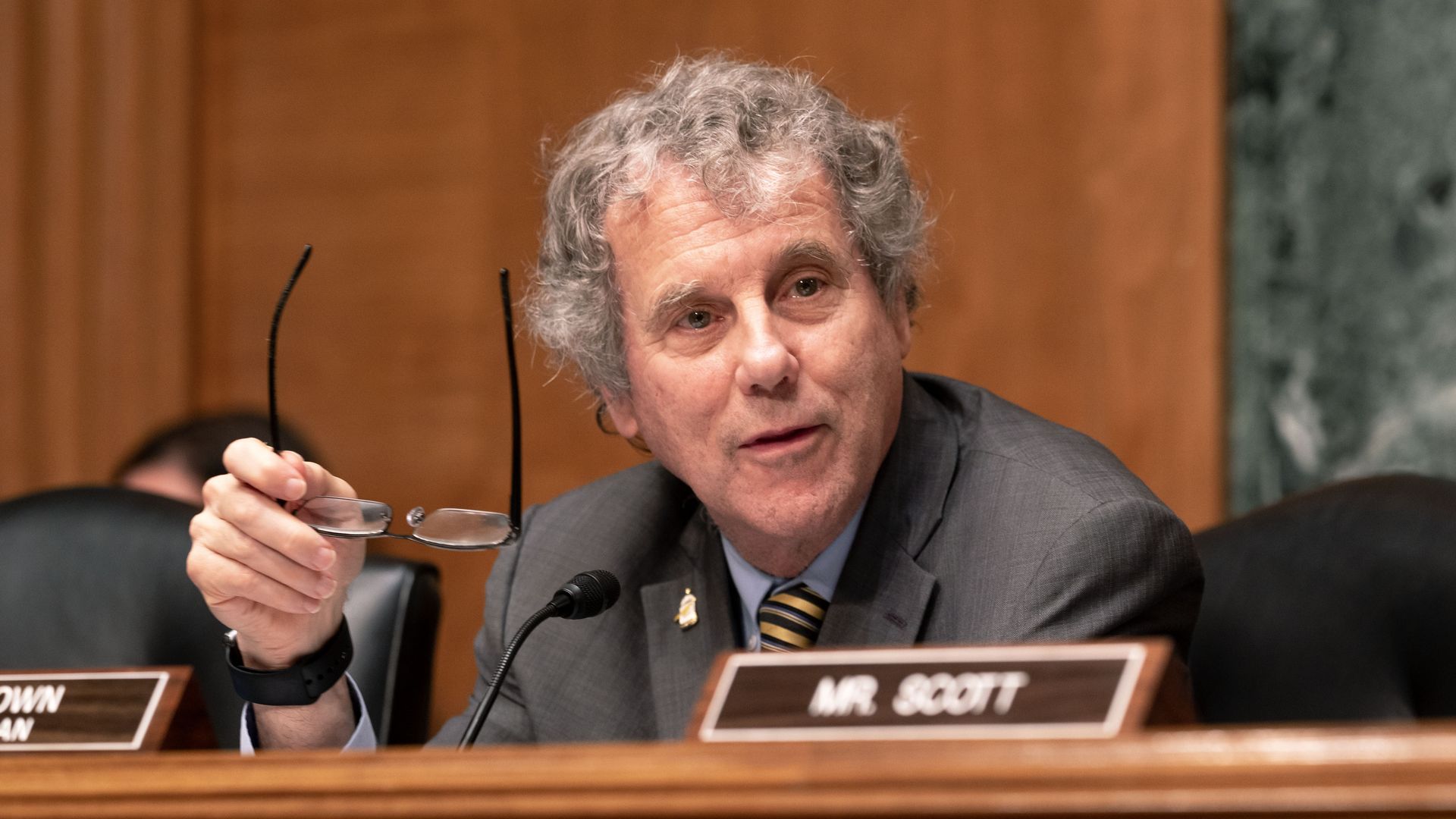 U.S. Senator Sherrod Brown at a committee hearing holding his glasses. 