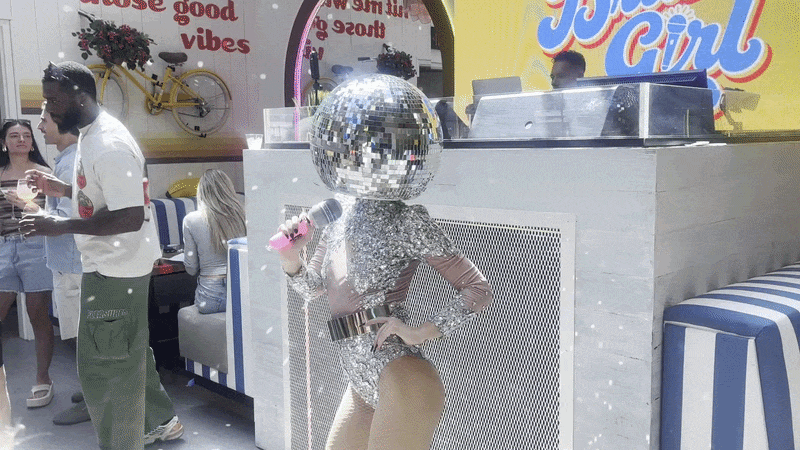 A dancer with a mic and a disco ball on her head. 
