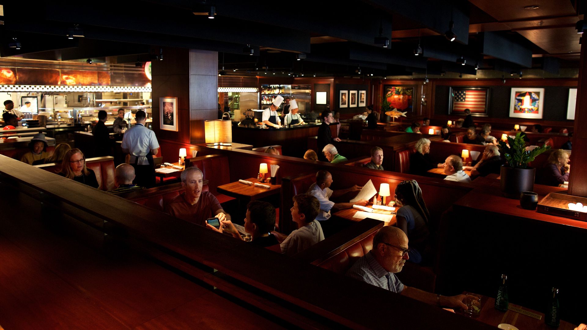 Woodmont Grill dimly lit dining room with booths and table lamps, and a view into the kitchen. Photo by Deb Lindsey for The Washington Post via Getty Images).