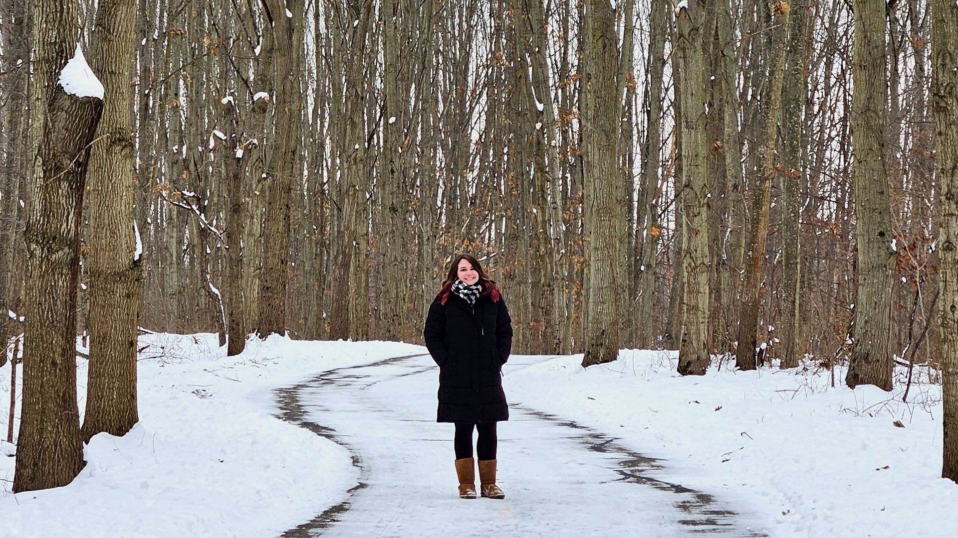 Alissa stands on a snowy path surrounded by tall trees