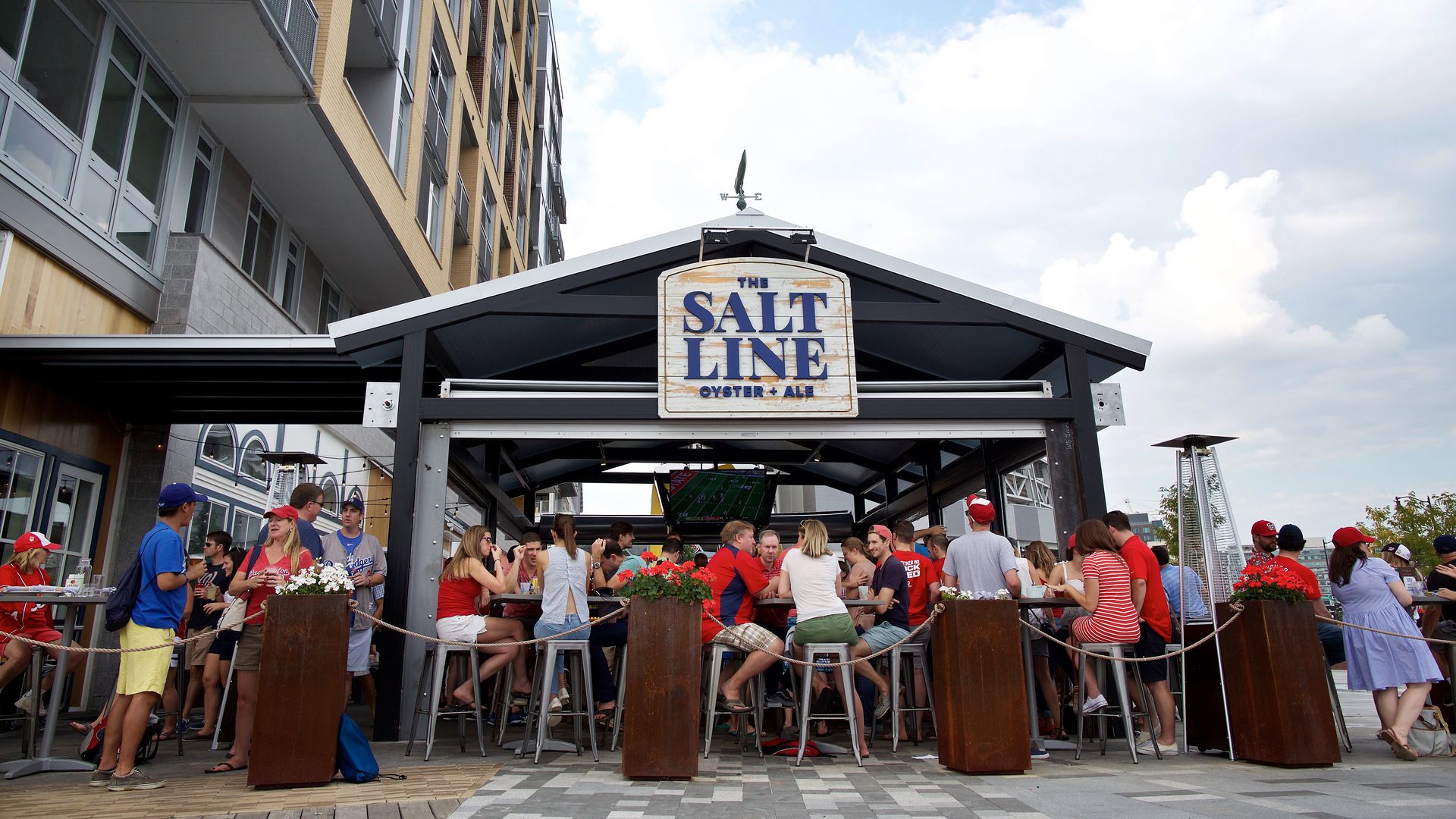 An outdoor bar full of baseball fans in red shirts