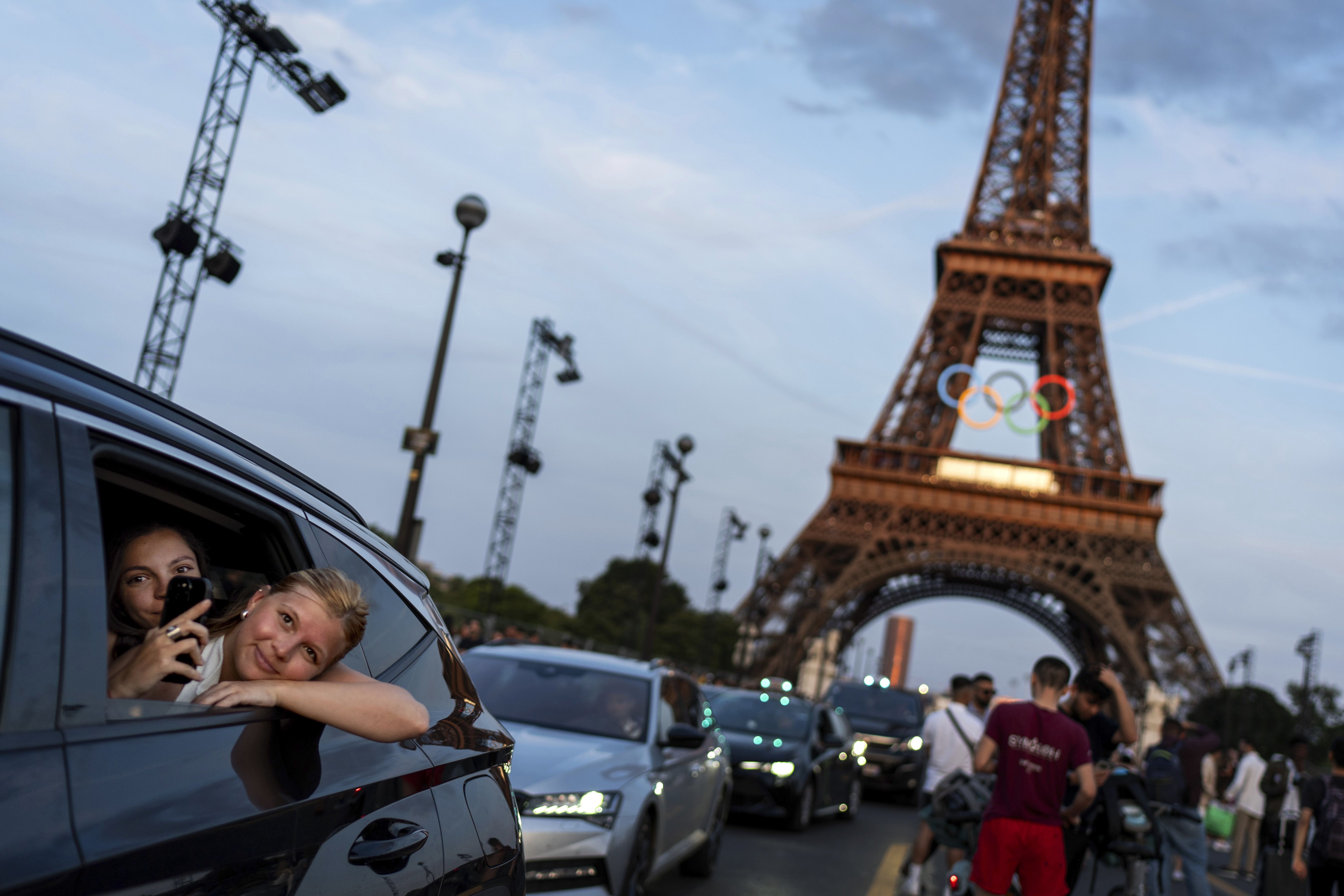 Passengers in the back of a taxi film themselves in front of the Eiffel Tower decorated for the Olympics, which open next Friday in Paris.