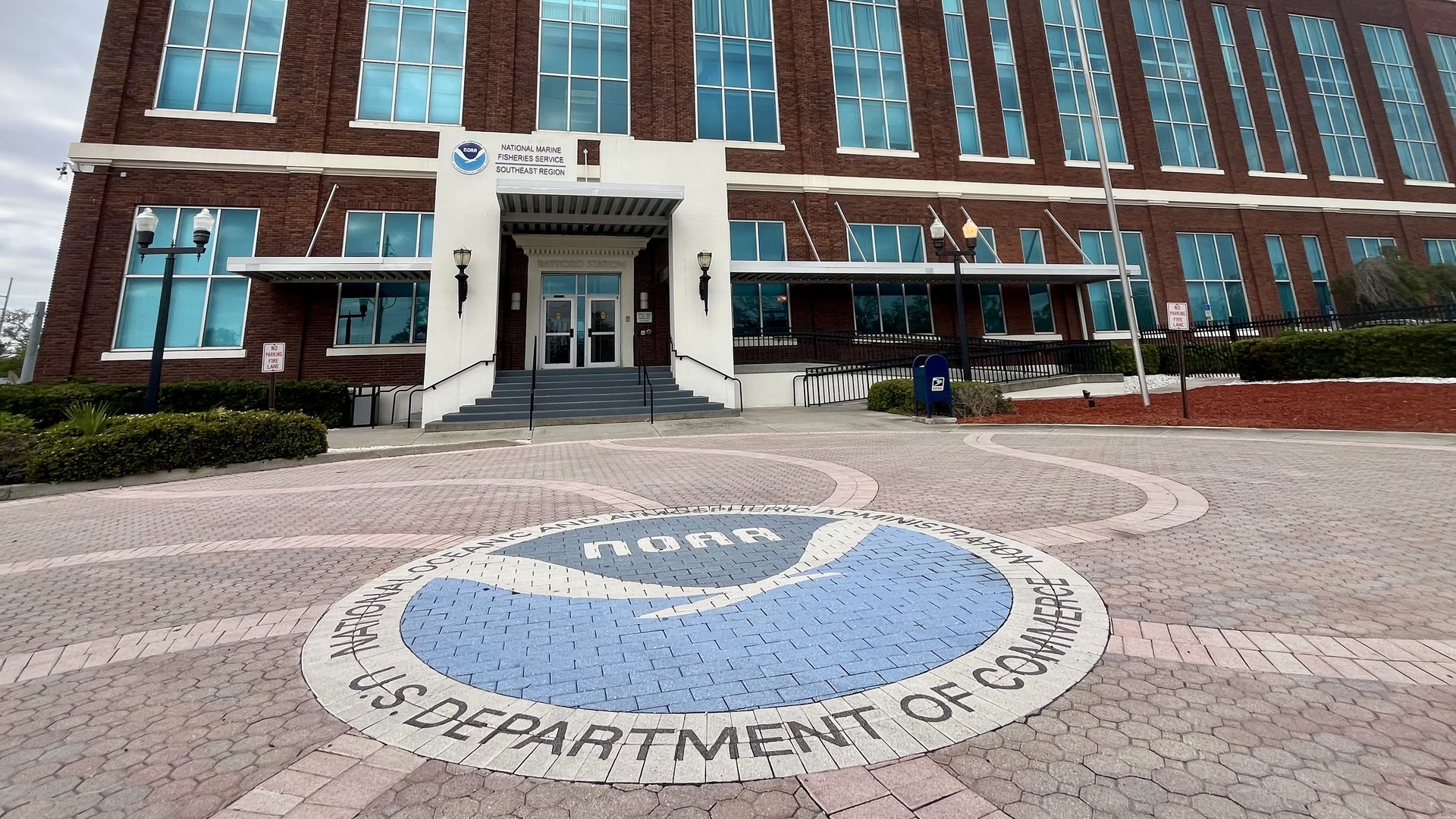 A brick building with a sign that says "National Marine Fisheries Service Southeast Region." A roundabout in front of the building features blue bricks creating the seal for NOAA.