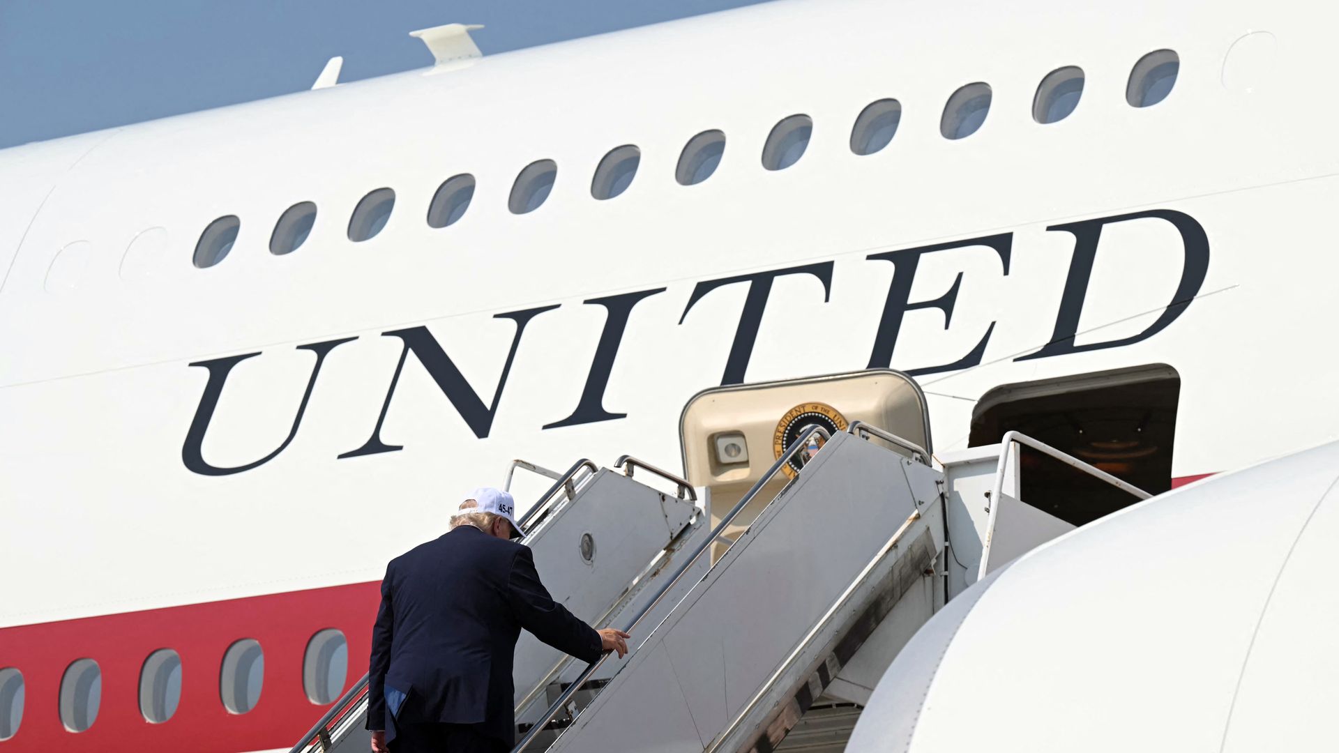 Trump wears a suit and a white hat as he climbs stairs to enter Air Force One.
