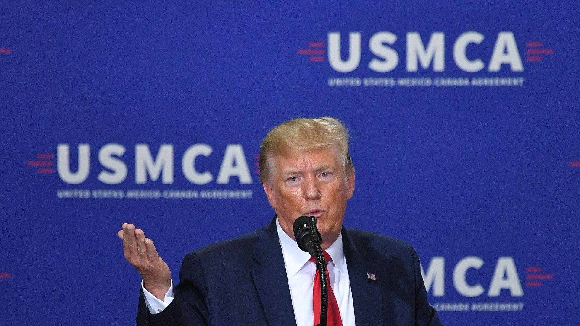 President Trump in front of a blue sign with white letters that says USMCA.
