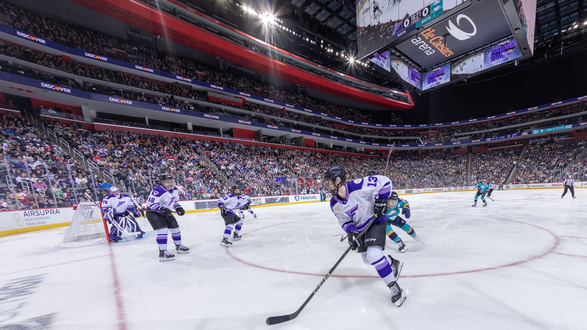 Hockey players on the ice. LCA logo visible above and big crowd watching