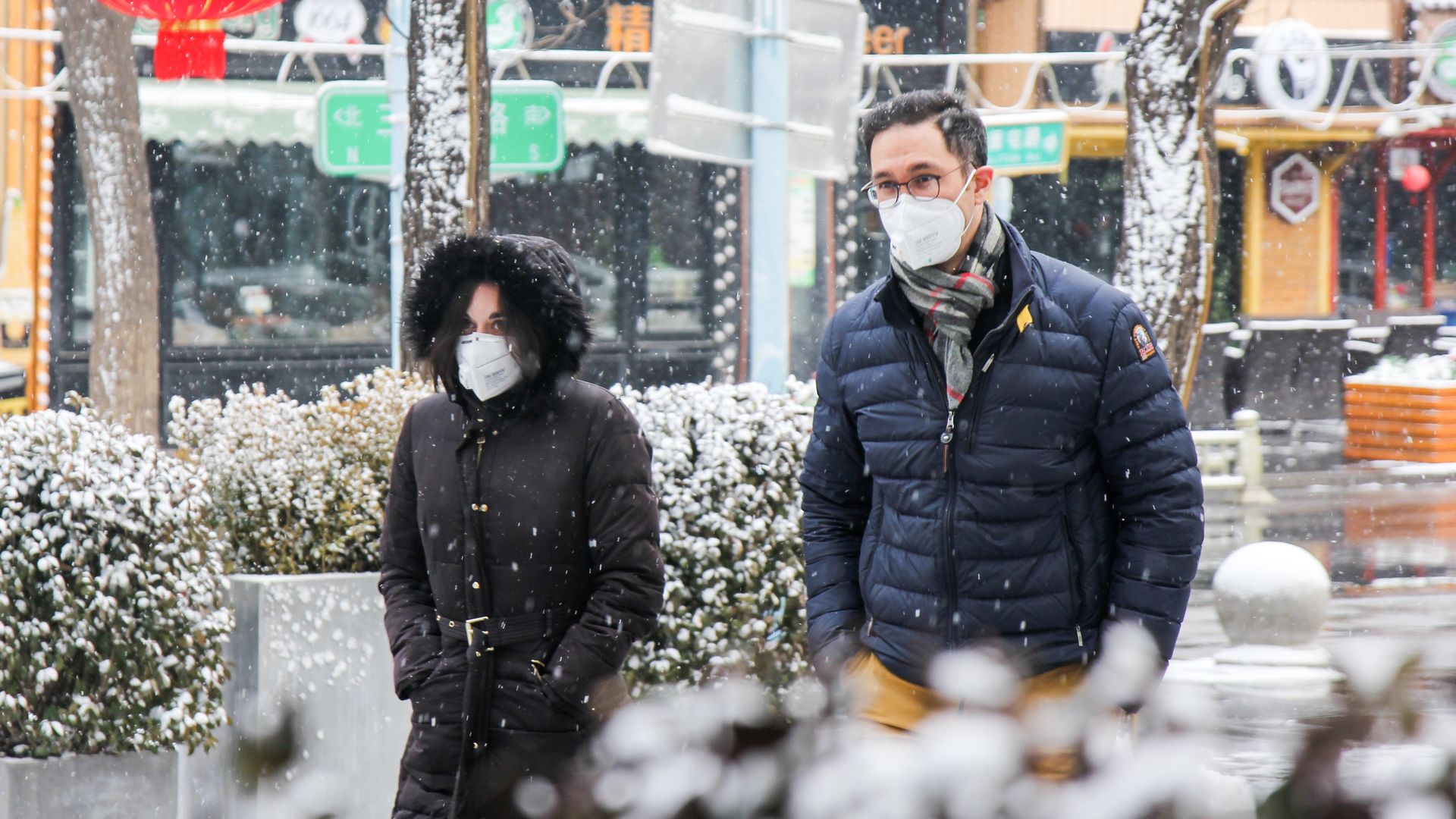 In this image, two people wear face masks while walking down the street in Beijing.