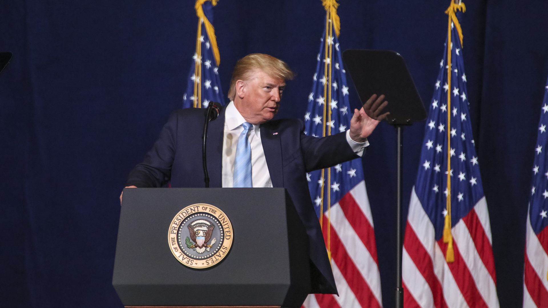 In this image, Trump waves while standing in front of several American flags.