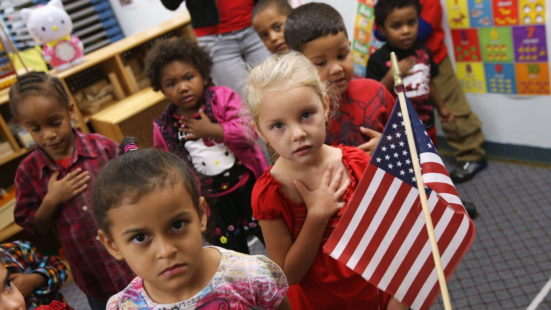 A classroom with small children reciting the Pledge of Allegiance. 