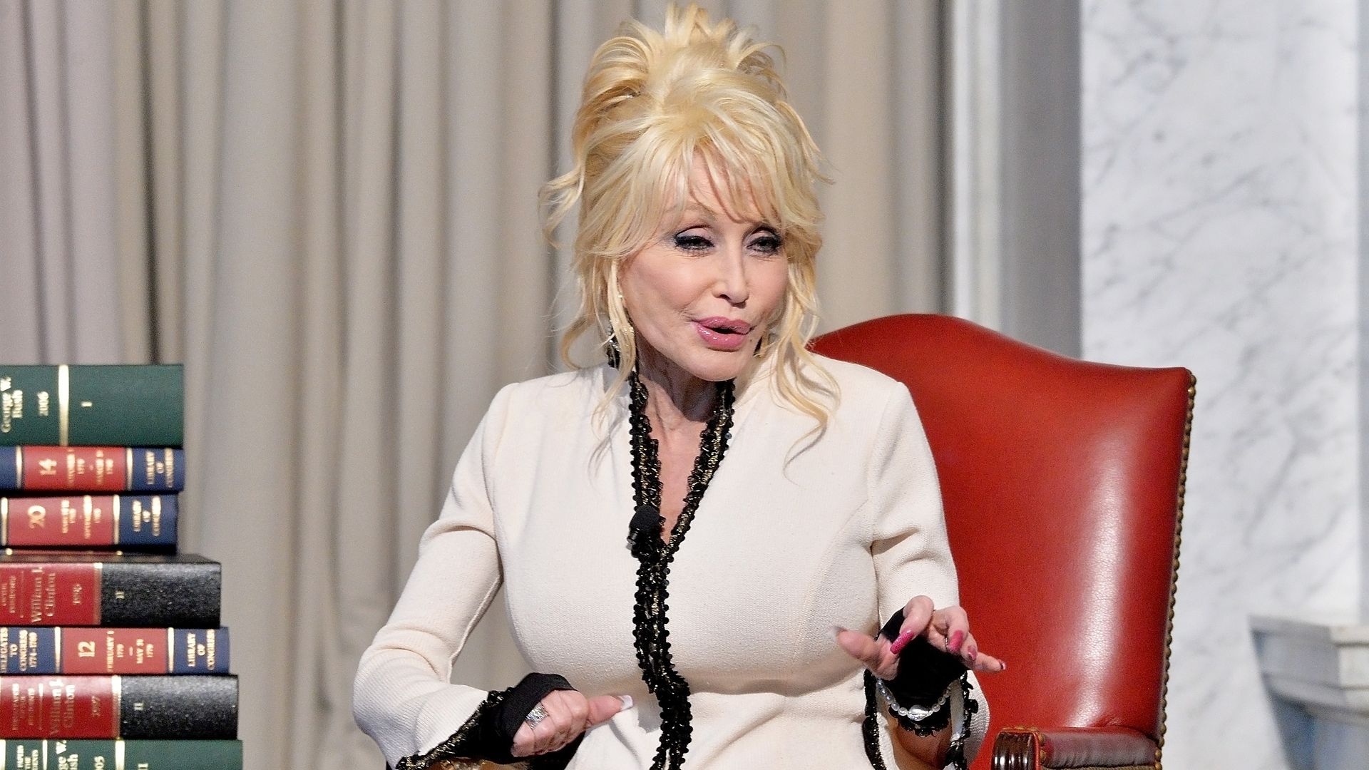 Dolly Parton speaks, sitting next to books.