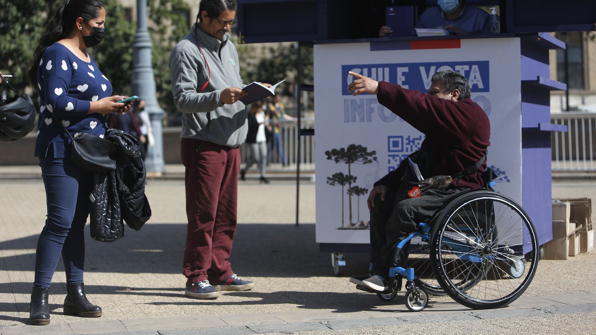 A man in a wheelchair directs two people standing outside in Chile
