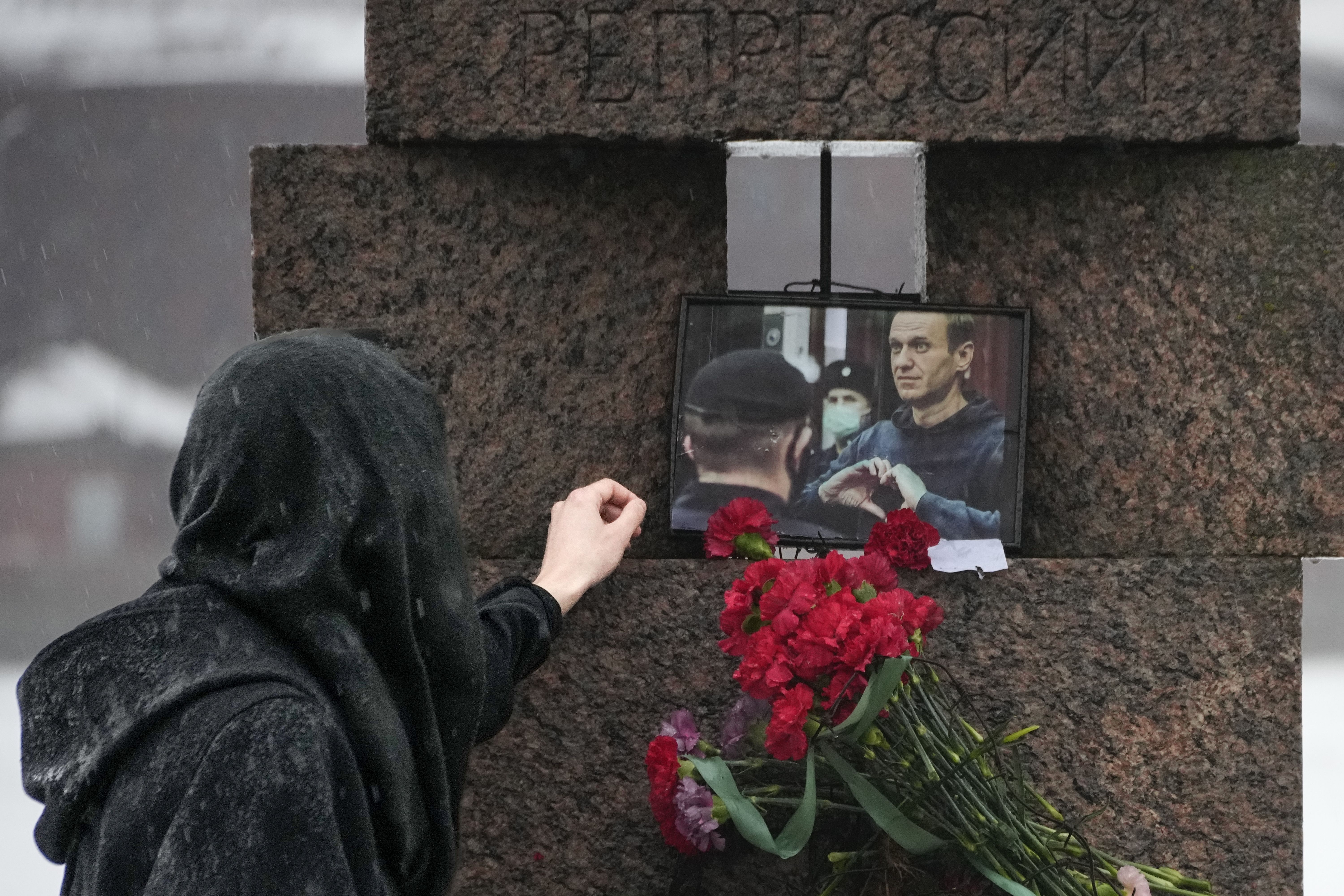 A woman touches a photo of Alexei Navalny after laying flowers at a memorial in St. Petersburg.