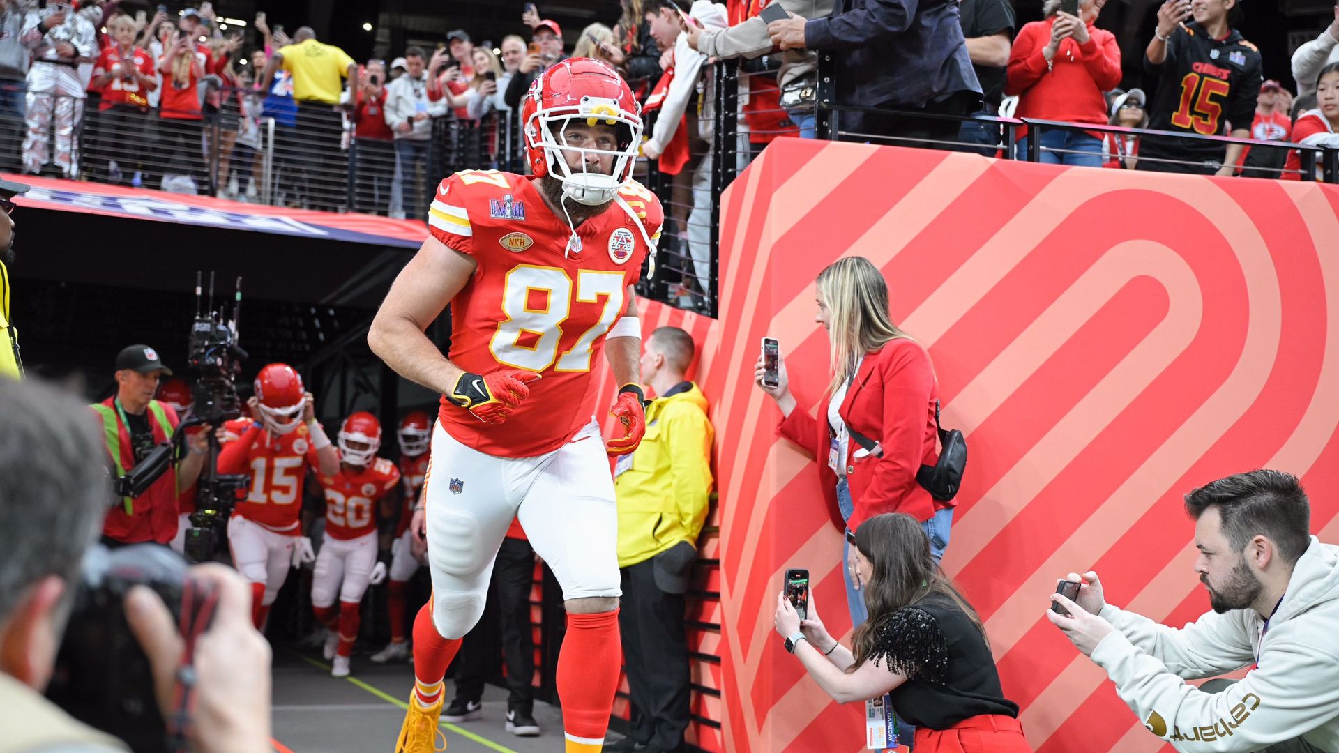 A man in a red and white football uniform and helmet runs out of a  tunnel