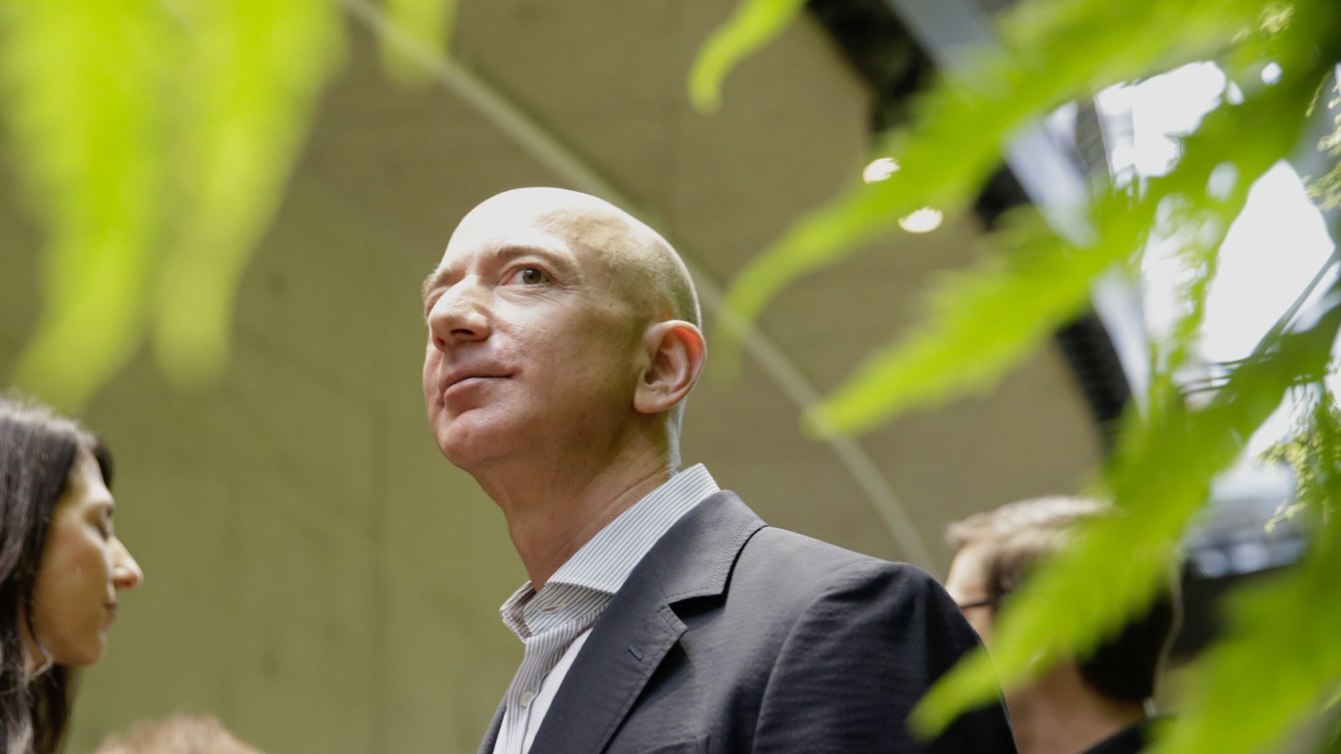 Jeff Bezos in focus in the background, with a green plant, out of focus, framing him in the foreground