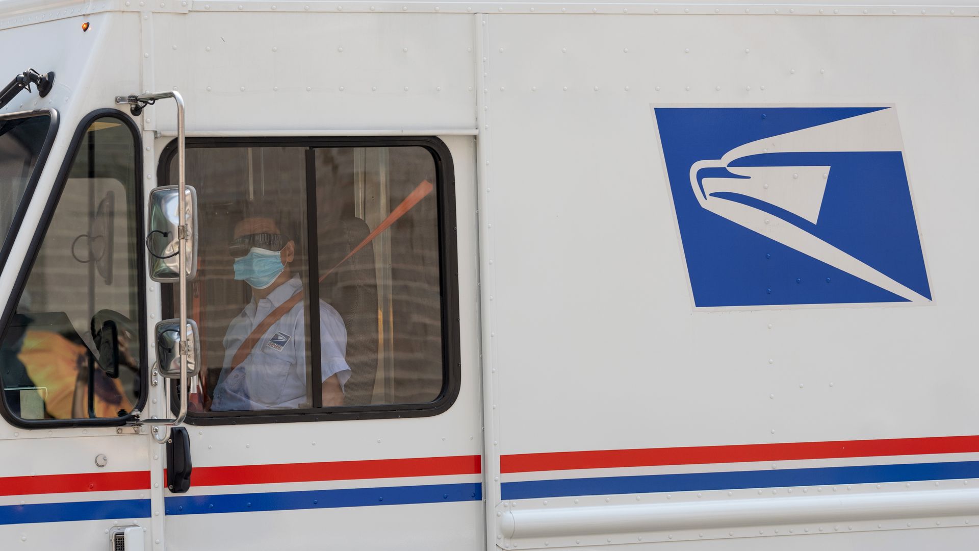 A mail worker wearing a mask looks out the window while driving