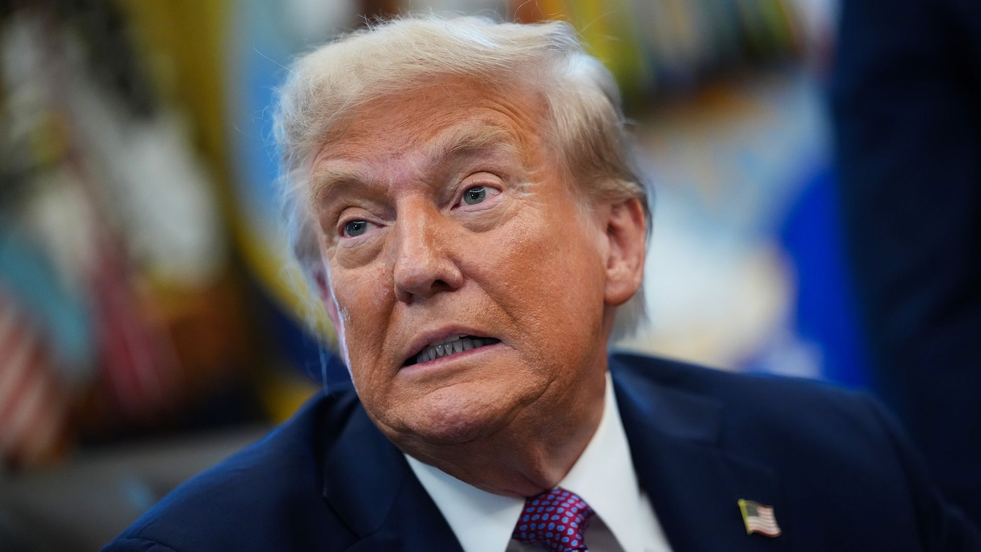 President Trump speaks to reporters while signing executive orders at his desk in the Oval Office.