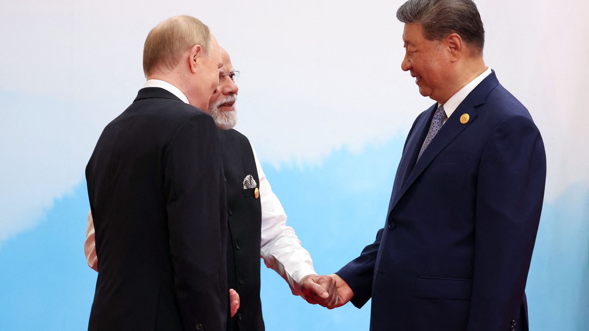 Three men, the leaders of Russia, India and China, shake hands. They are wearing dark suits.