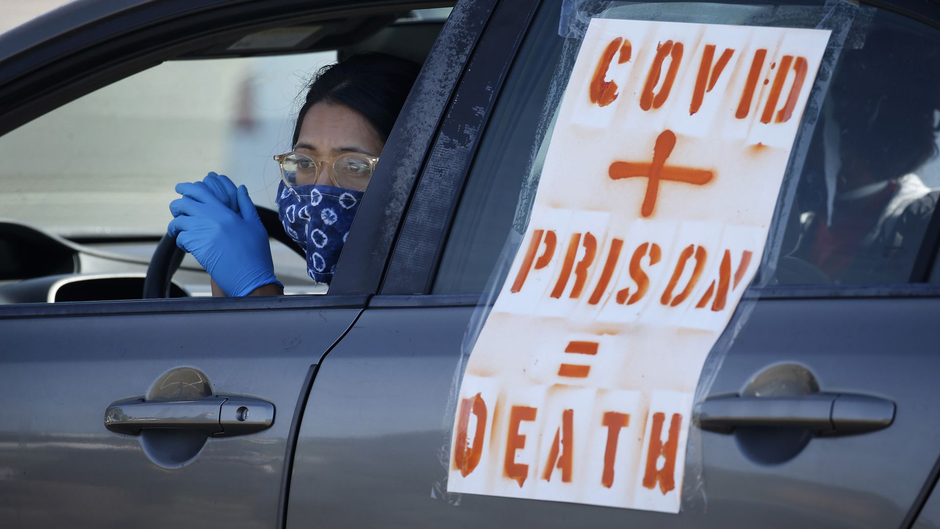 A demonstrator waits in her car with a poster that says "COVID + Prison = Death"