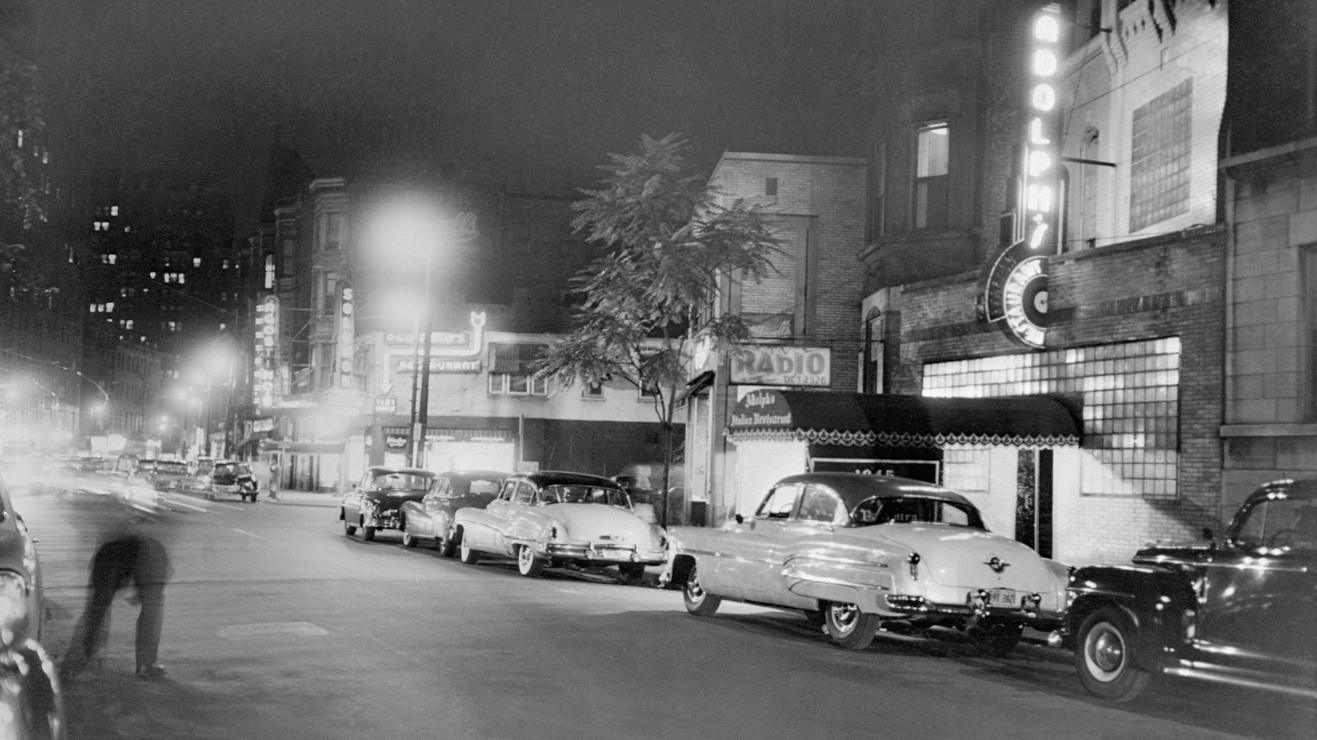 Photo of an old street with 1950s automobiles lining the parking spaces.